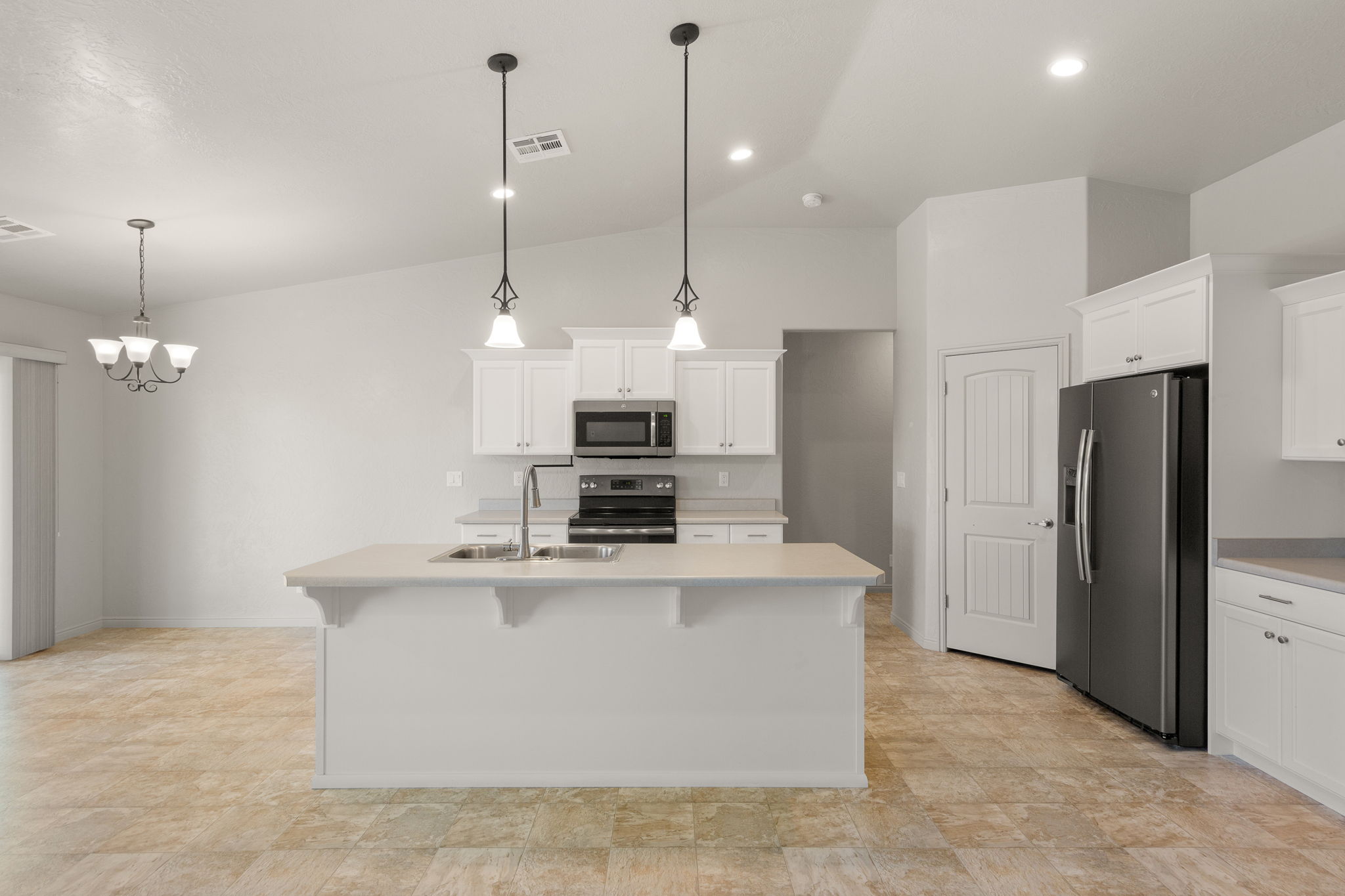 Open-concept kitchen featuring an island with an integrated sink, white cabinetry, dark stainless steel appliances, and recessed lighting