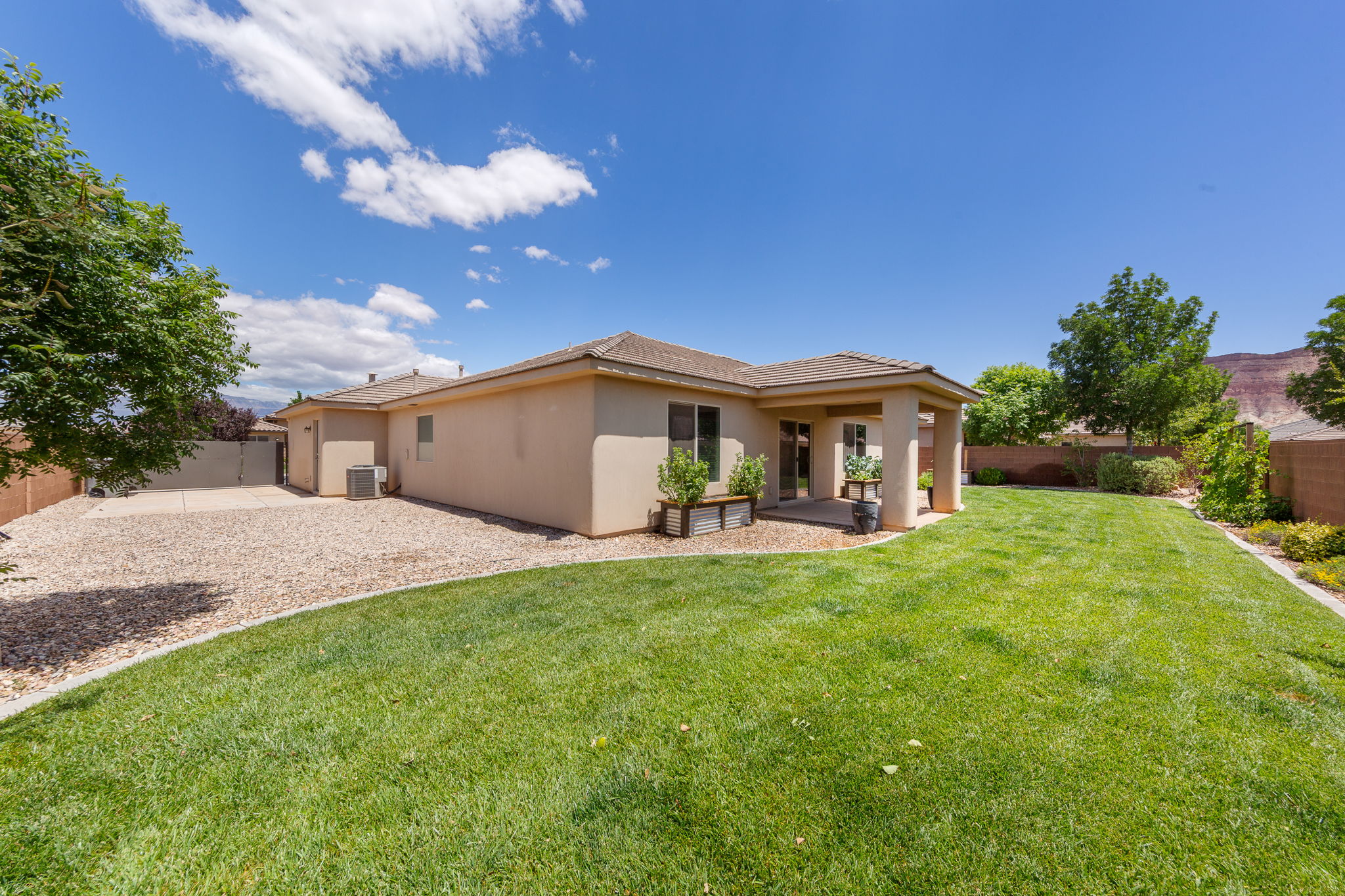 Expansive rear yard featuring a large grass lawn, a covered patio area, and a gravel-covered side yard