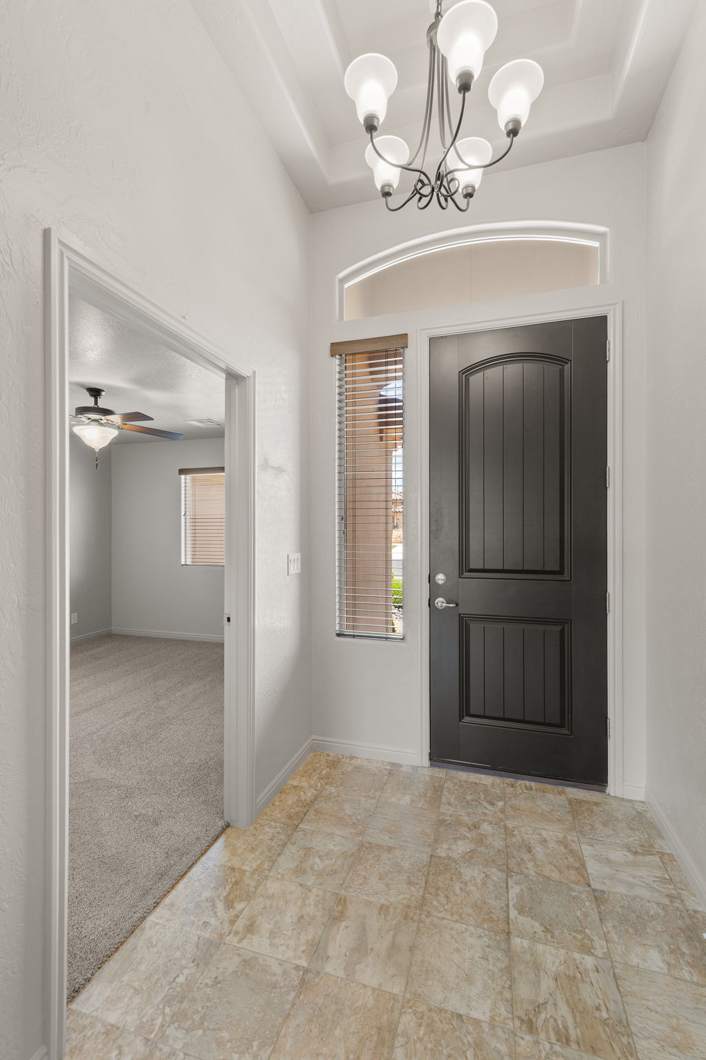Entryway featuring a dark paneled door with an arched transom window, a five-light chandelier, a coffered ceiling, and large format tile flooring
