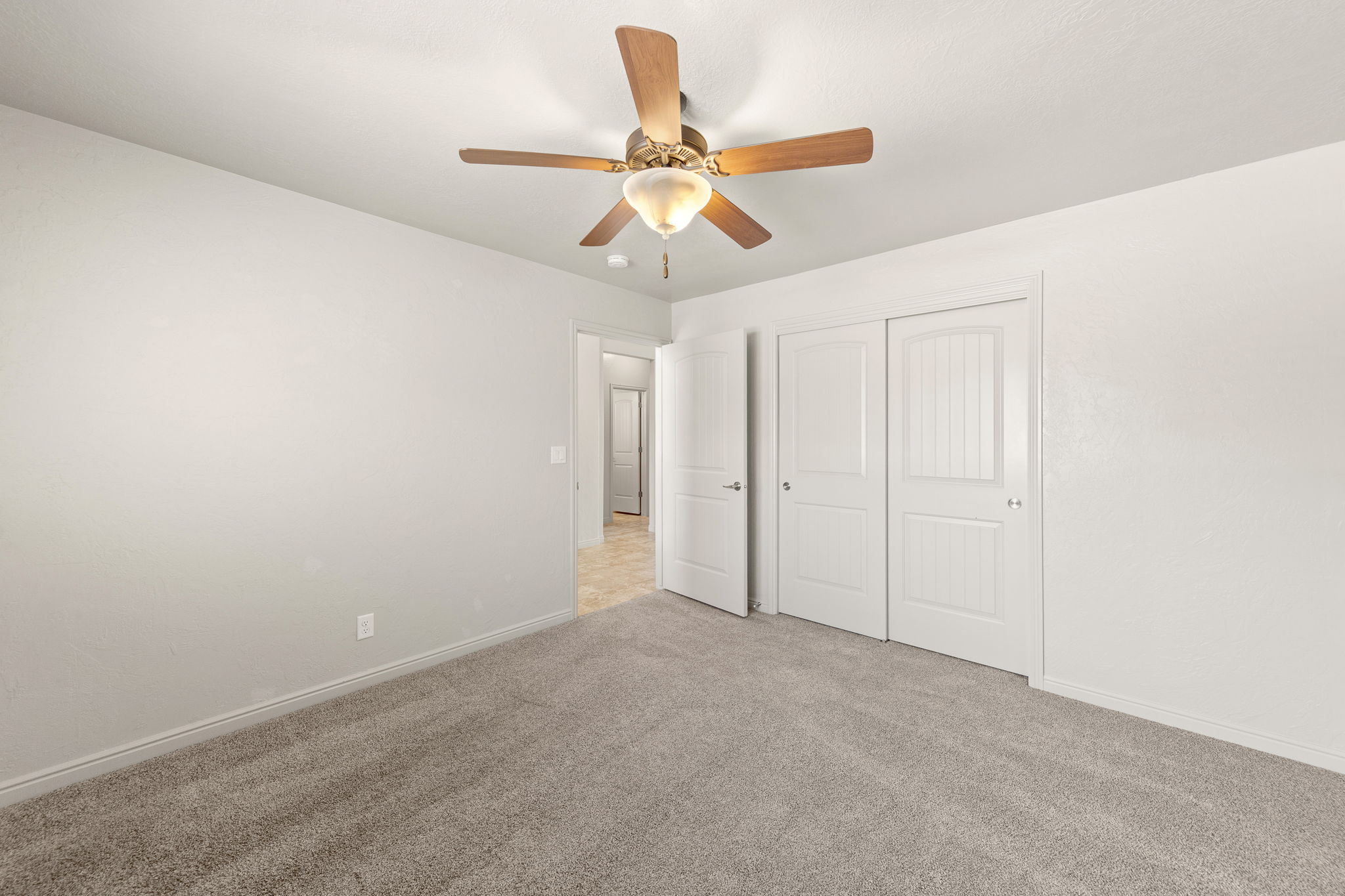Carpeted room featuring a ceiling fan with light fixture, white walls, and white bi-fold closet doors