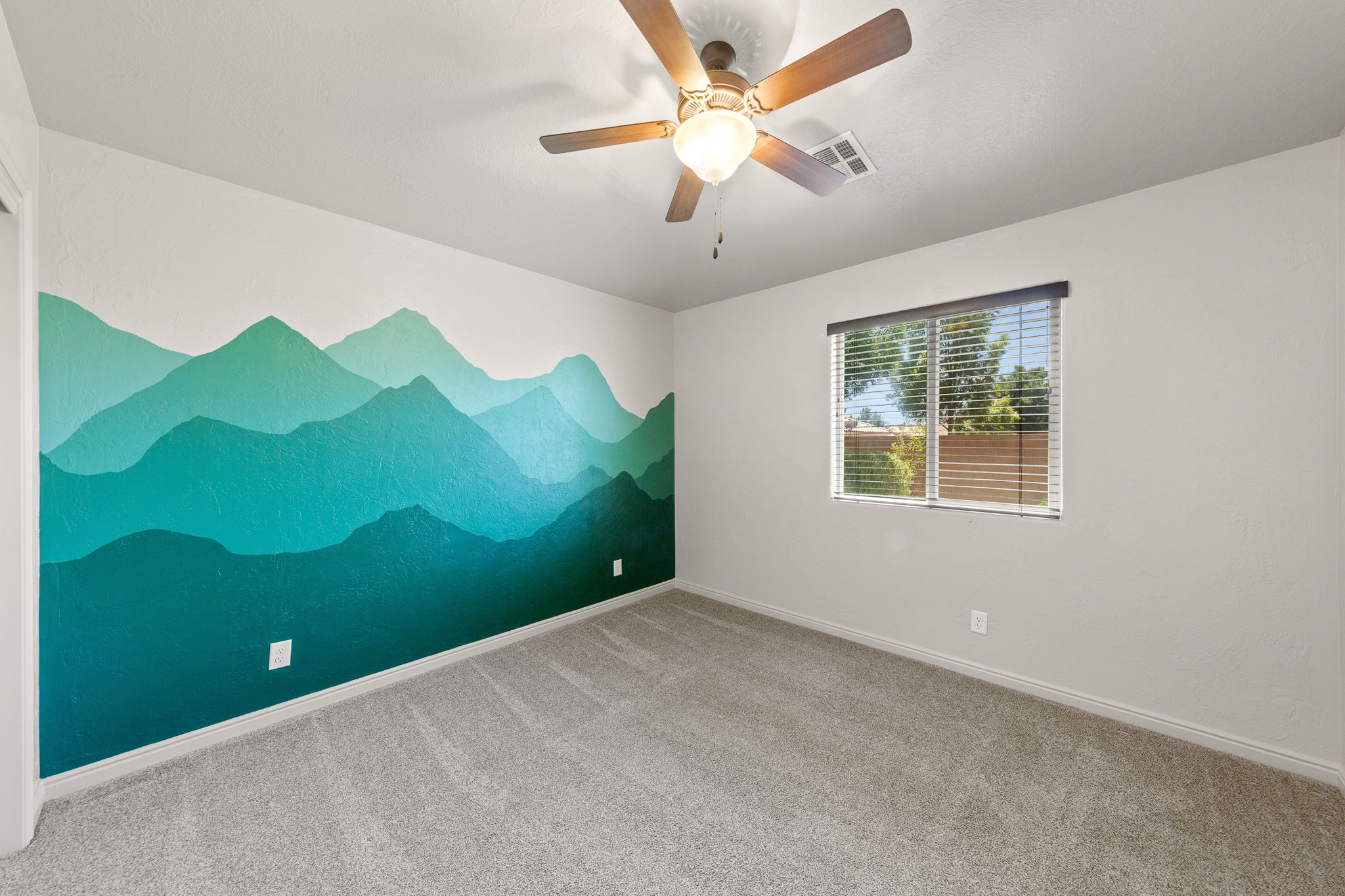Bedroom featuring a decorative mountain mural accent wall and light gray carpeting