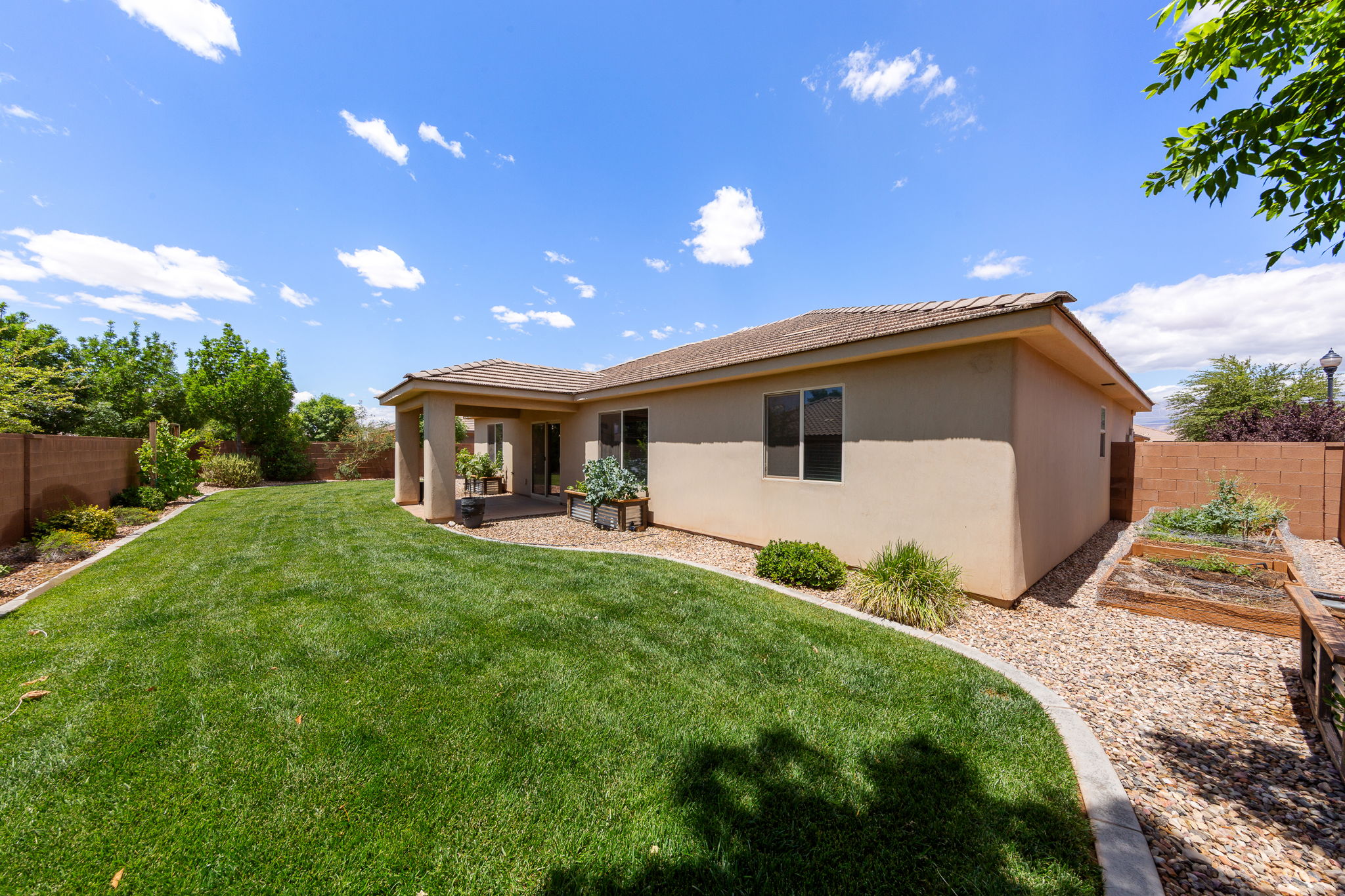 Expansive backyard featuring a manicured lawn, a covered patio, and a dedicated garden bed area