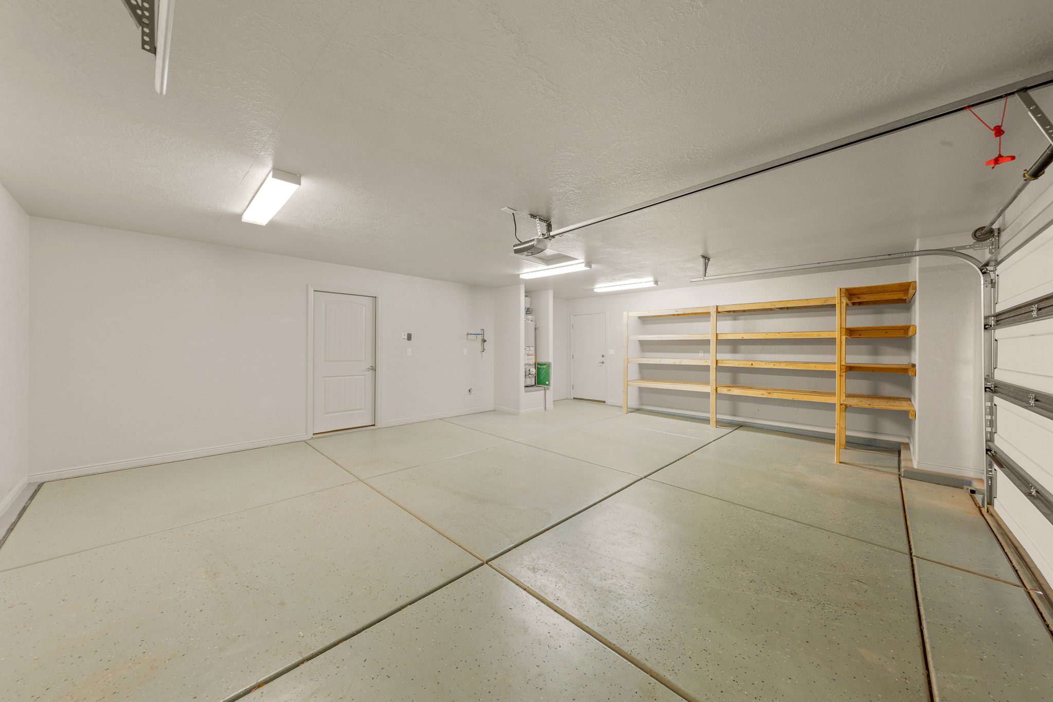 Spacious garage featuring a durable concrete floor, built-in shelving, white walls, overhead lighting fixtures, and an automatic garage door opener