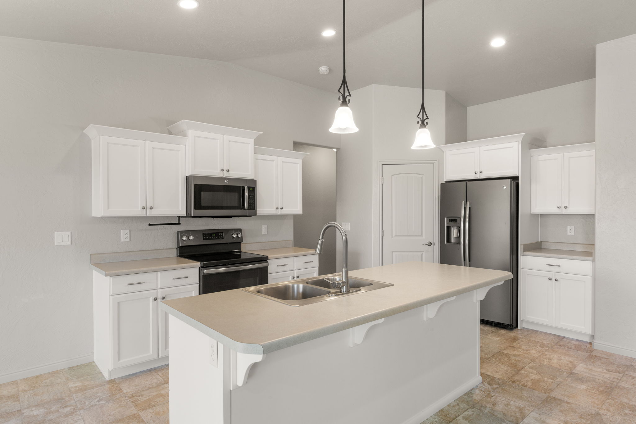 Kitchen featuring a central island with a double basin sink, white cabinetry with crown molding, stainless steel appliances, recessed lighting, and tiled flooring