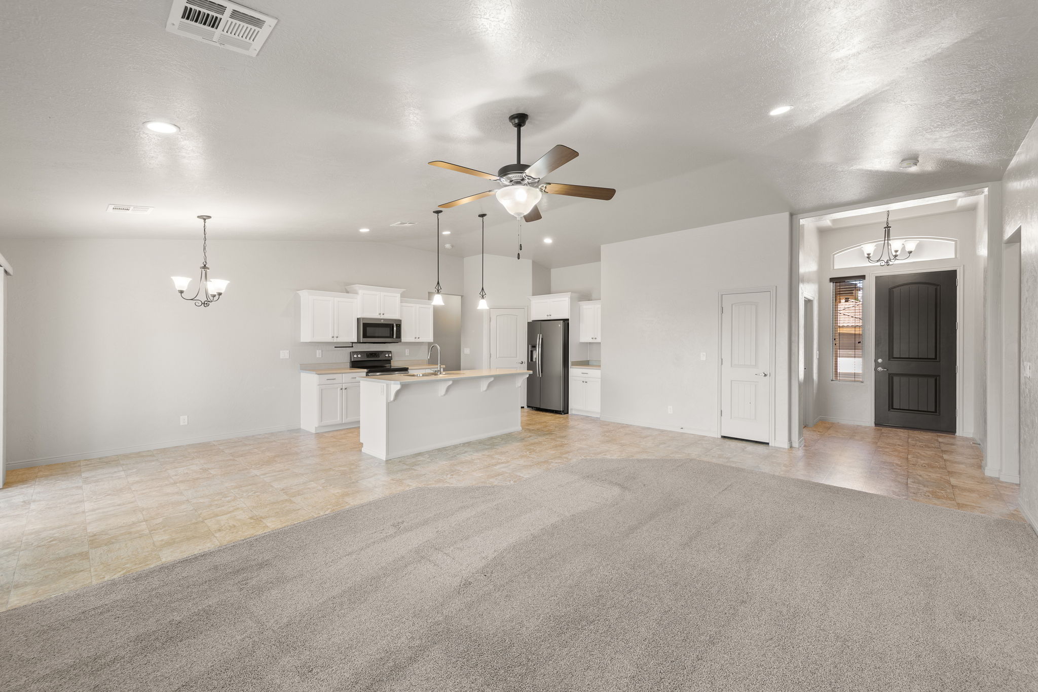 Open-concept living area featuring a kitchen with white cabinetry, stainless steel appliances, a center island with pendant lighting, and a neutral-toned countertop