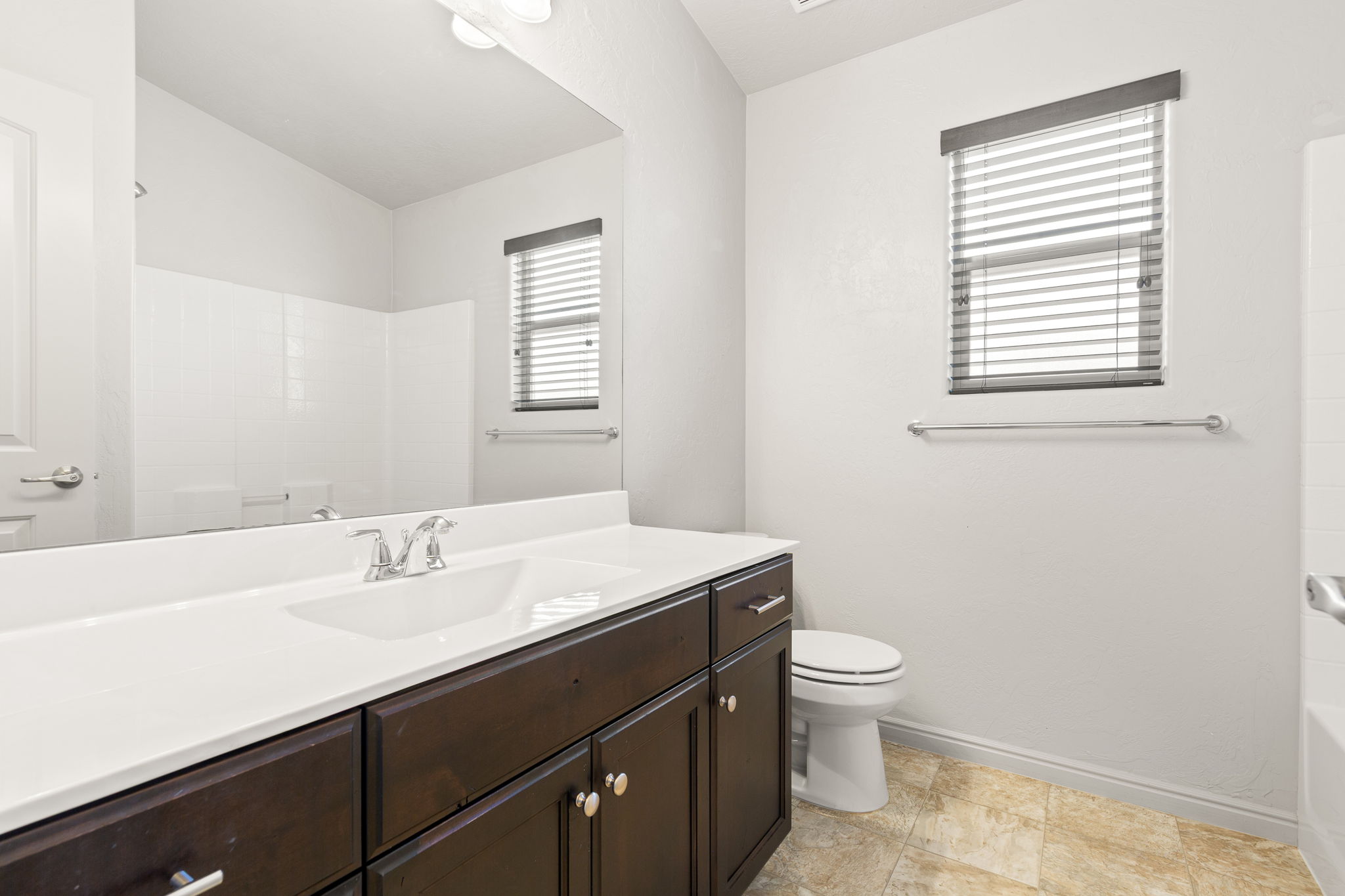 Bathroom featuring a dark wood-finish vanity with a white countertop and integrated sink, chrome faucet, and expansive mirror