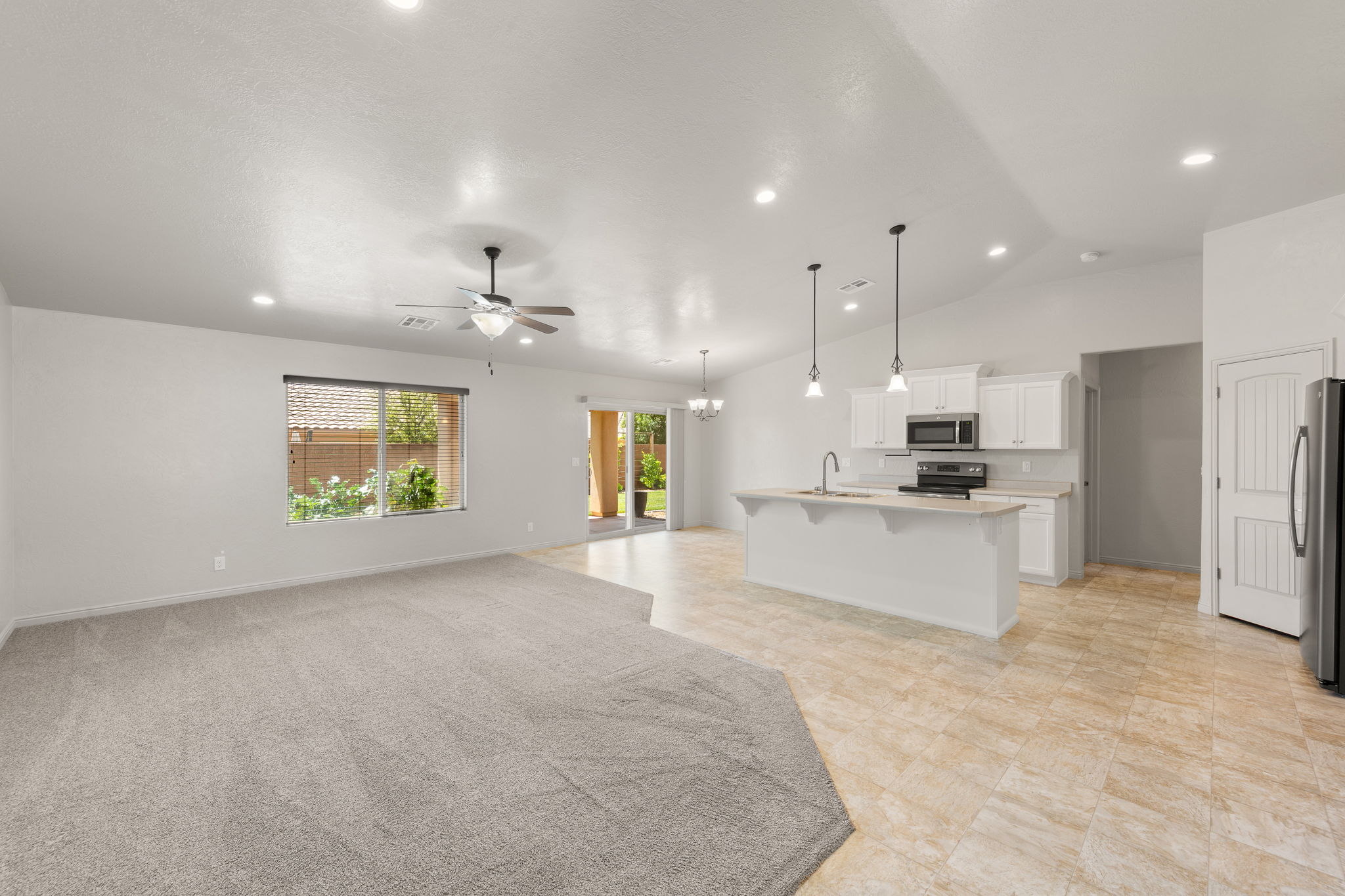 Open-concept kitchen and living area featuring a kitchen island with pendant lighting, white cabinetry, a built-in microwave, and tile flooring