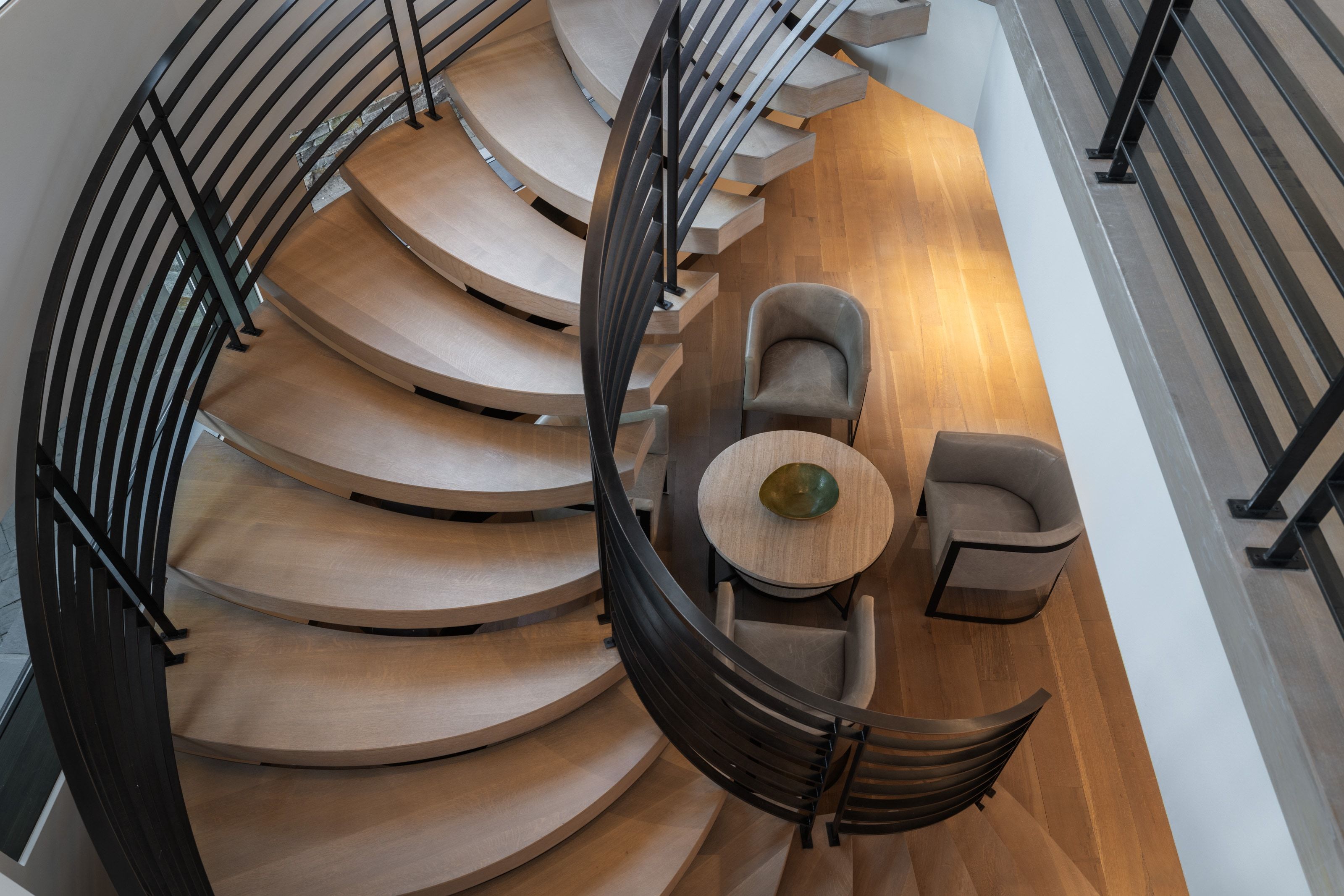 Curved wood-finish staircase with black metal railings, complemented by hardwood flooring