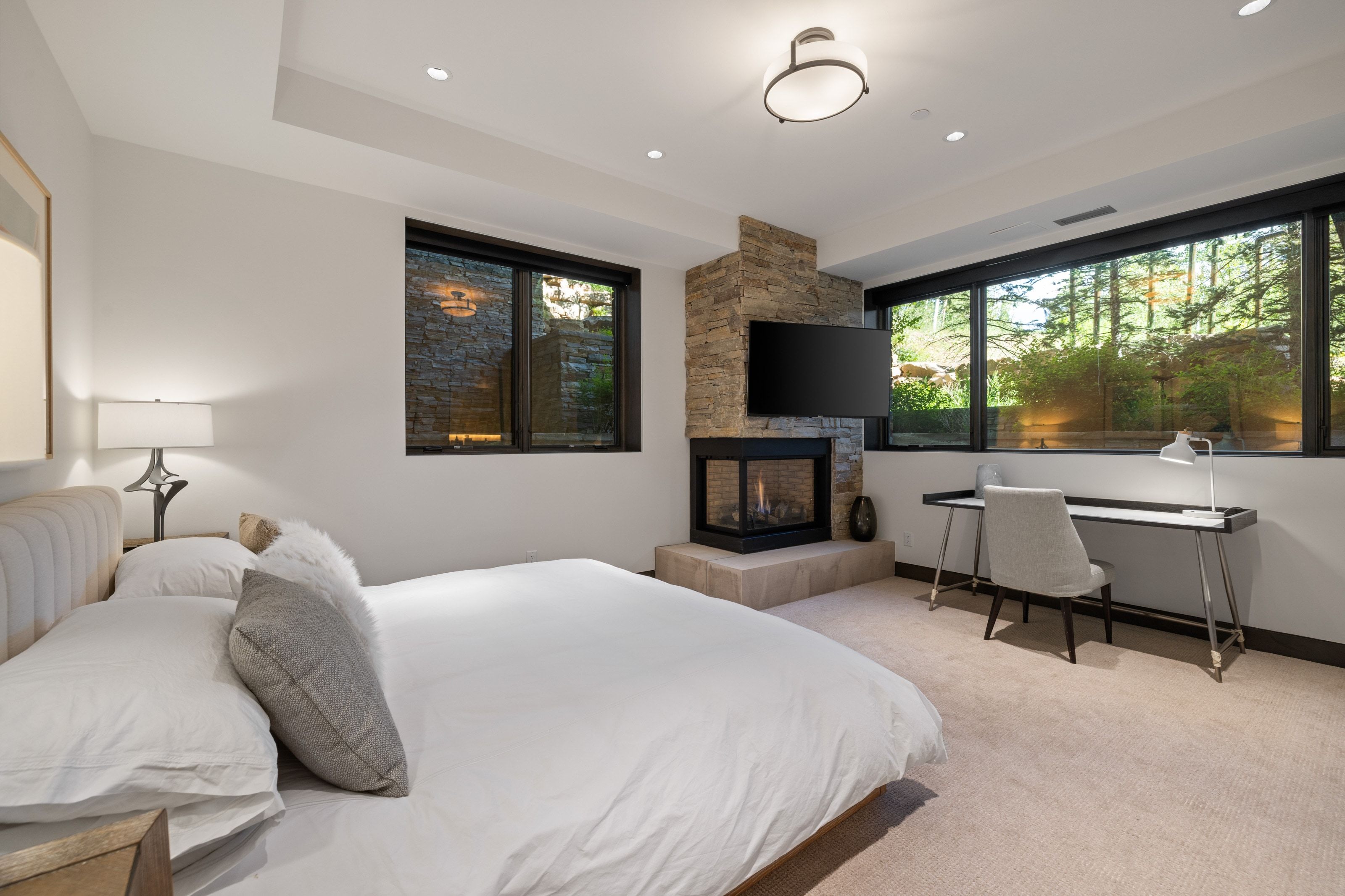 Bedroom featuring a stone-clad fireplace with a built-in television mount, a large picture window, and recessed lighting