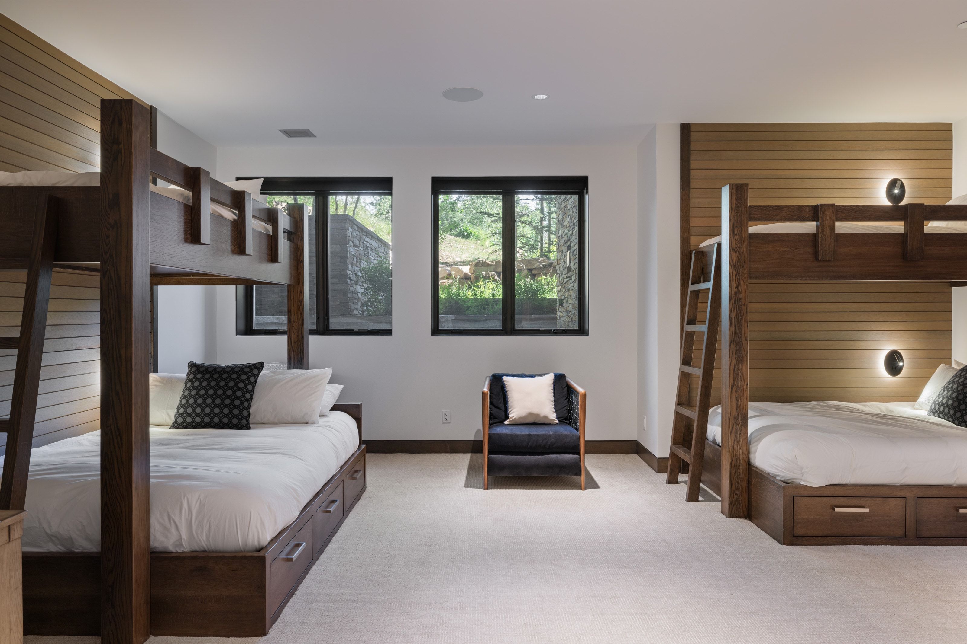 Spacious room featuring two dark wood bunk bed structures with integrated storage drawers, light wood paneling accents, and soft carpet flooring