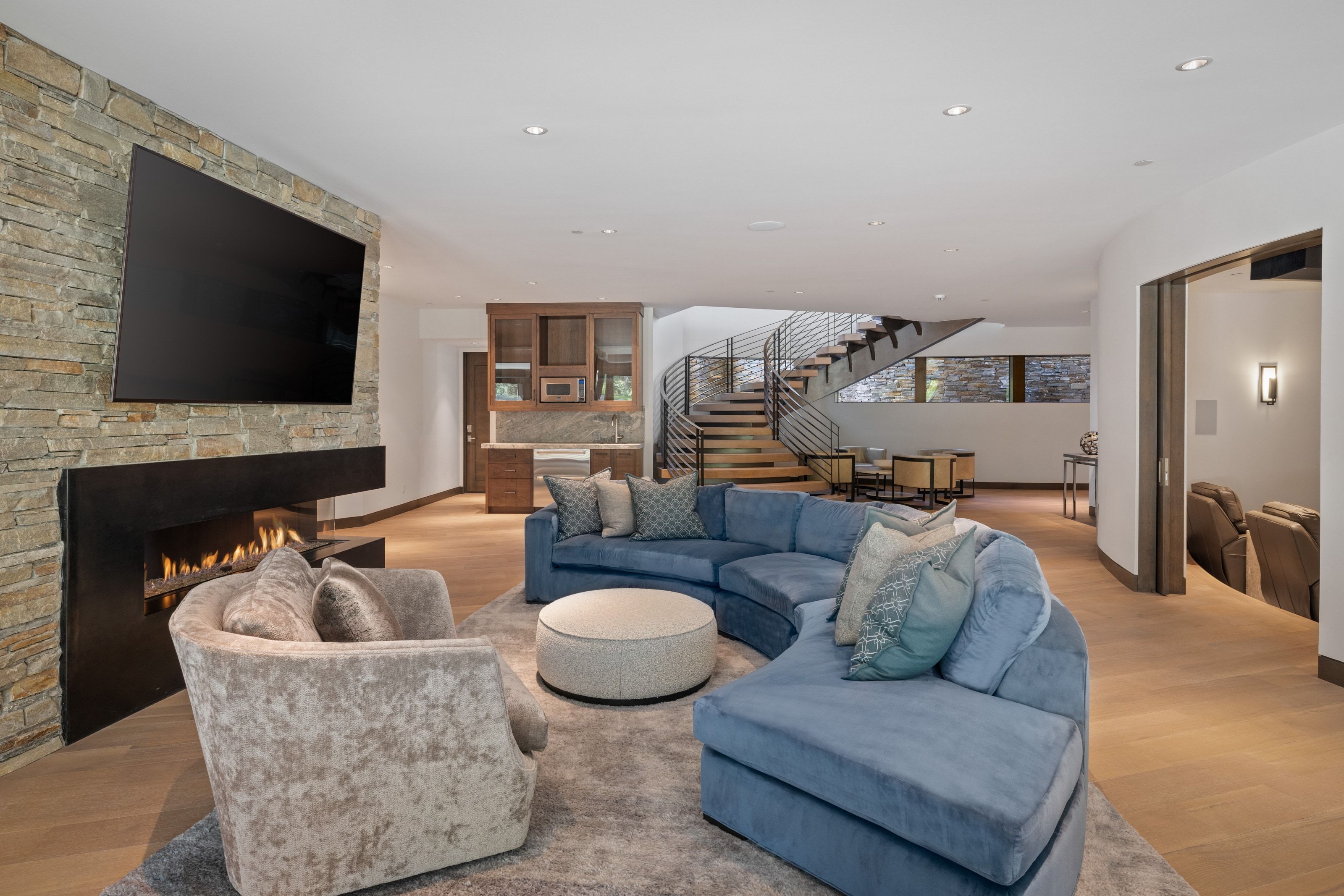 Spacious living area featuring a stone accent wall with a linear fireplace, recessed lighting, wood-finish flooring, a built-in wet bar with cabinetry, and a modern open staircase with metal railings