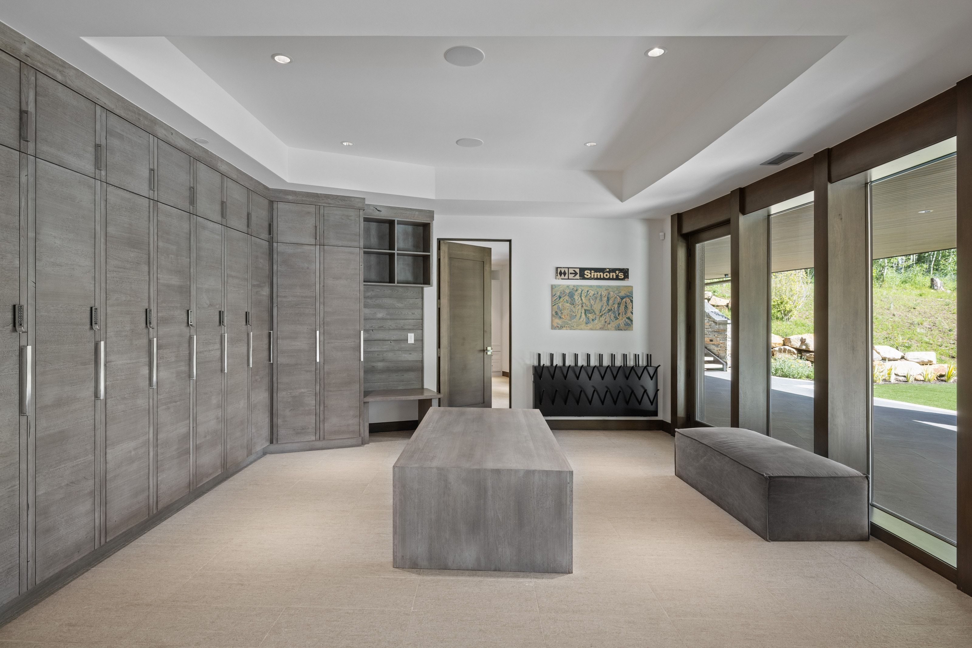 Spacious room featuring extensive built-in gray wood-finish cabinetry with silver hardware, recessed ceiling lighting, and large windows with dark wood framing