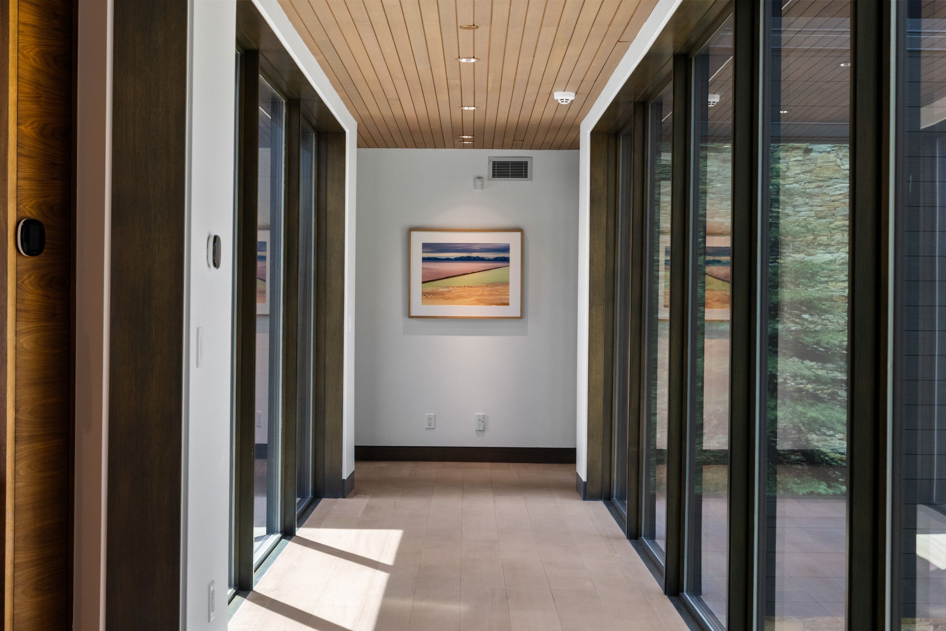 Hallway featuring light wood-finish flooring, a paneled wood ceiling, and floor-to-ceiling windows with dark frames