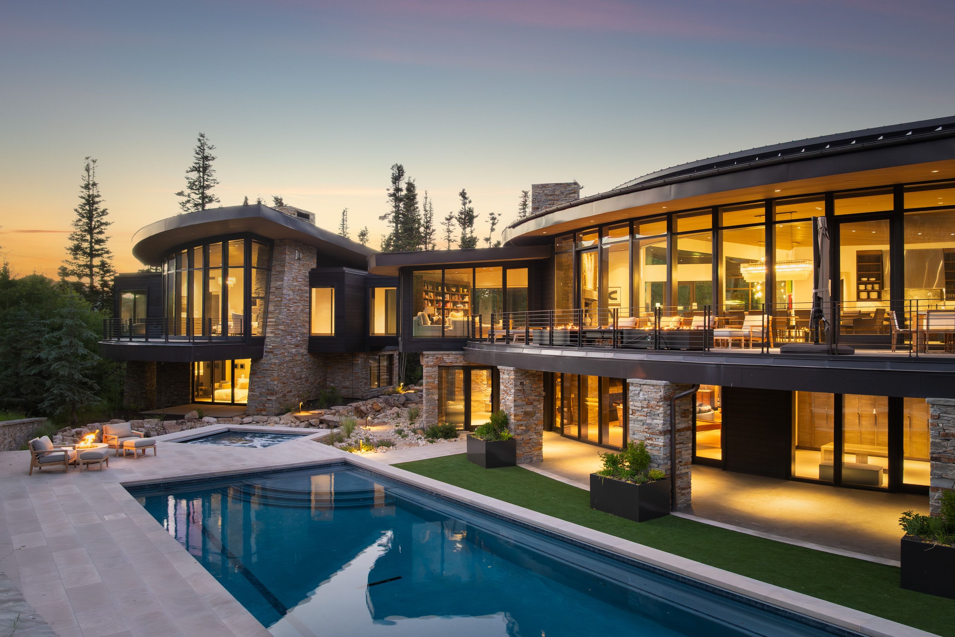 Modern architectural design featuring extensive glass walls, stone-clad exterior accents, a multi-level deck, a swimming pool, and a separate spa