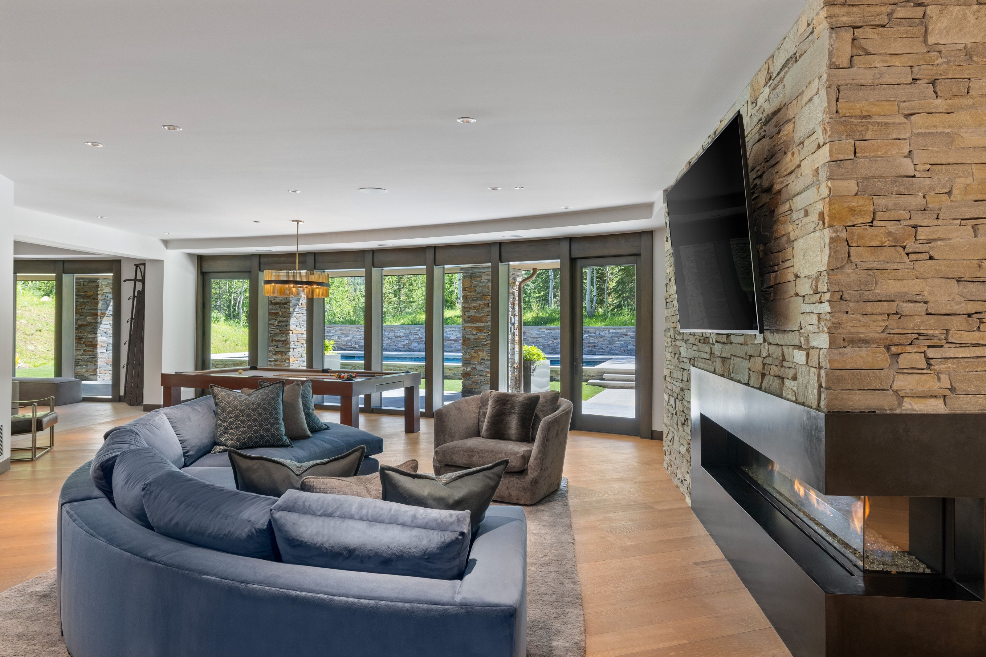 Spacious living area featuring a stacked stone fireplace with a modern linear insert, wood-finish flooring, and multiple glass doors opening to the exterior