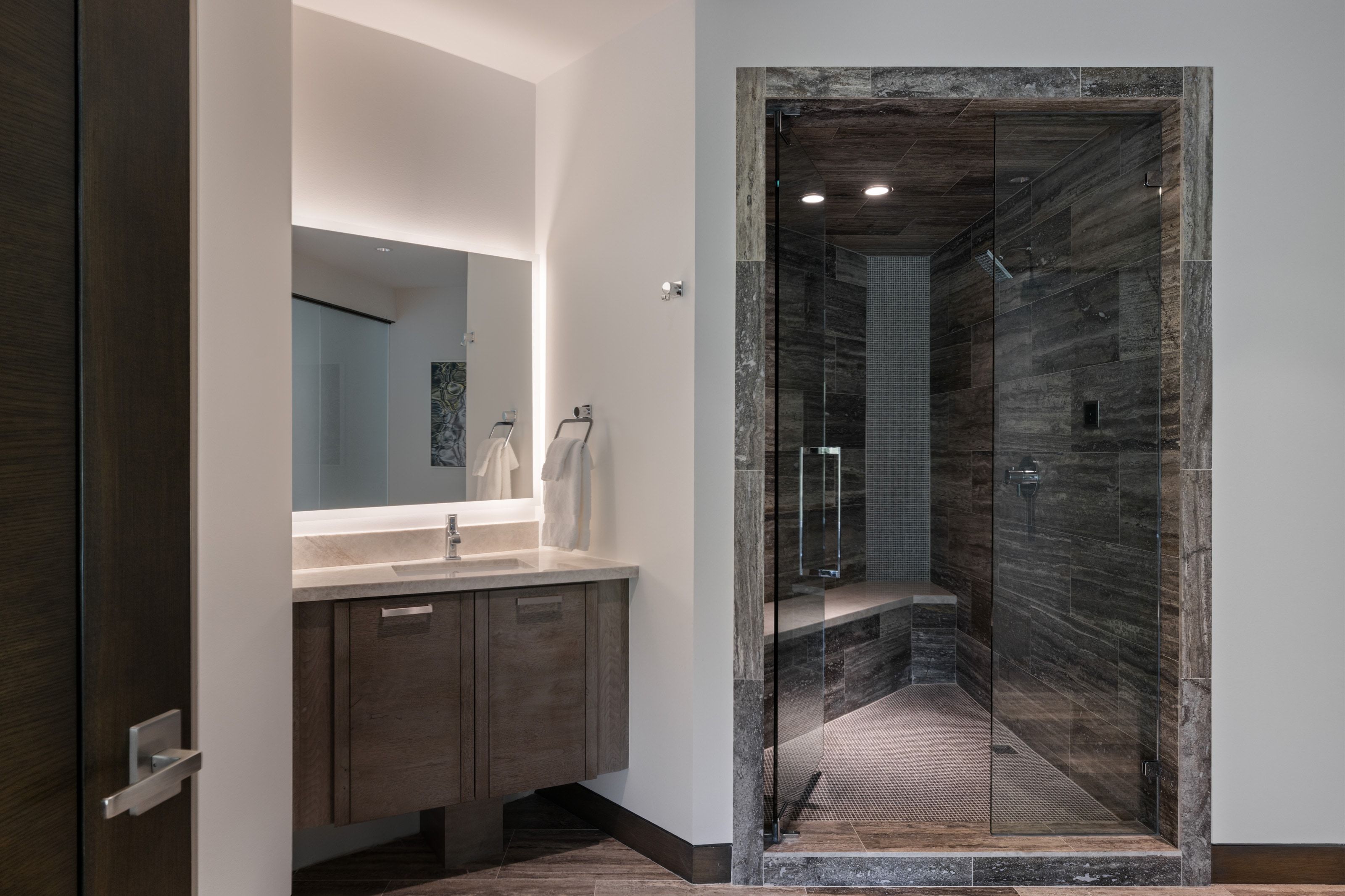 Walk-in glass shower enclosure with dark stone tile surround and integrated bench