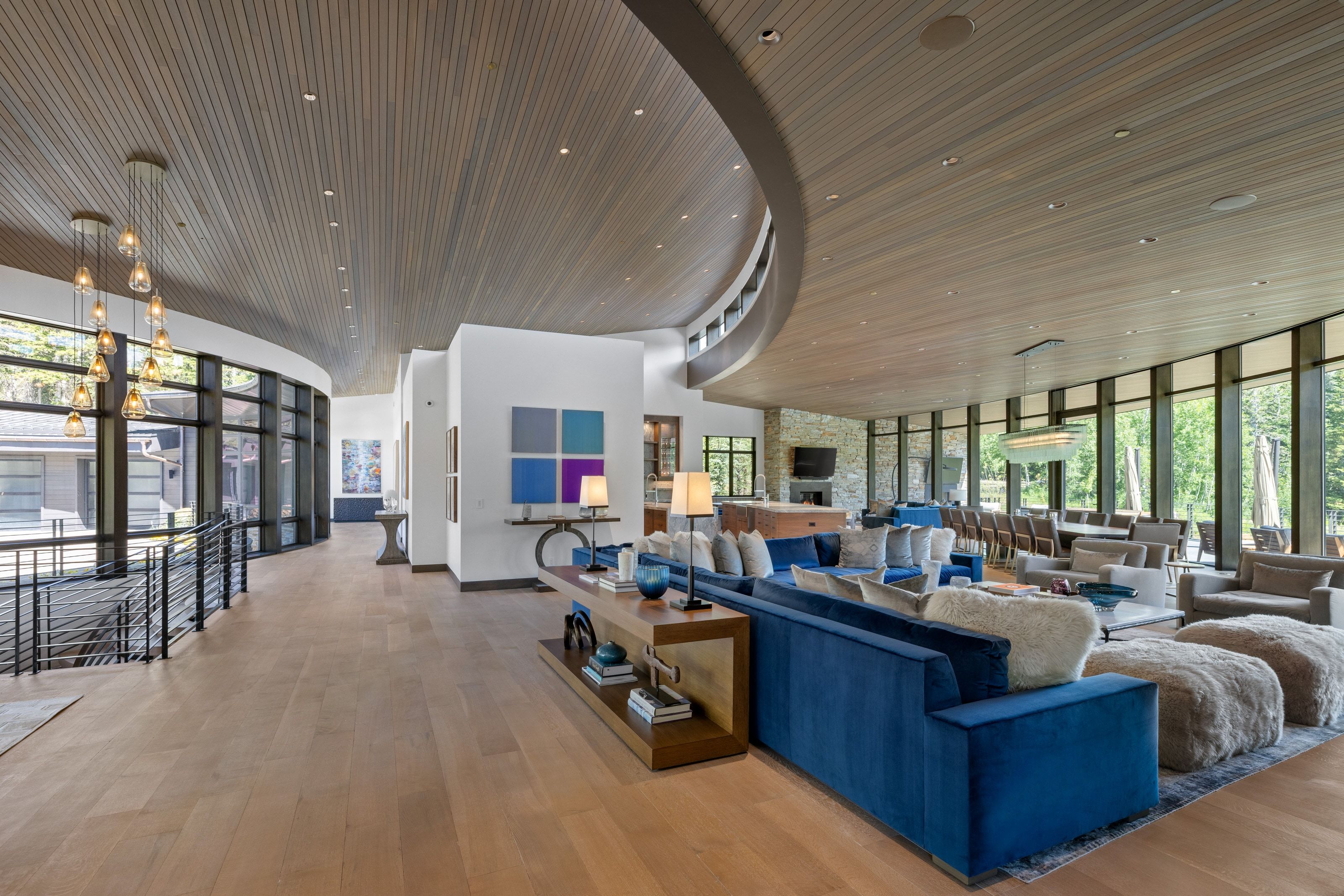 Spacious open-concept interior with light wood-finish flooring, a curved wood-panel ceiling, and extensive floor-to-ceiling windows