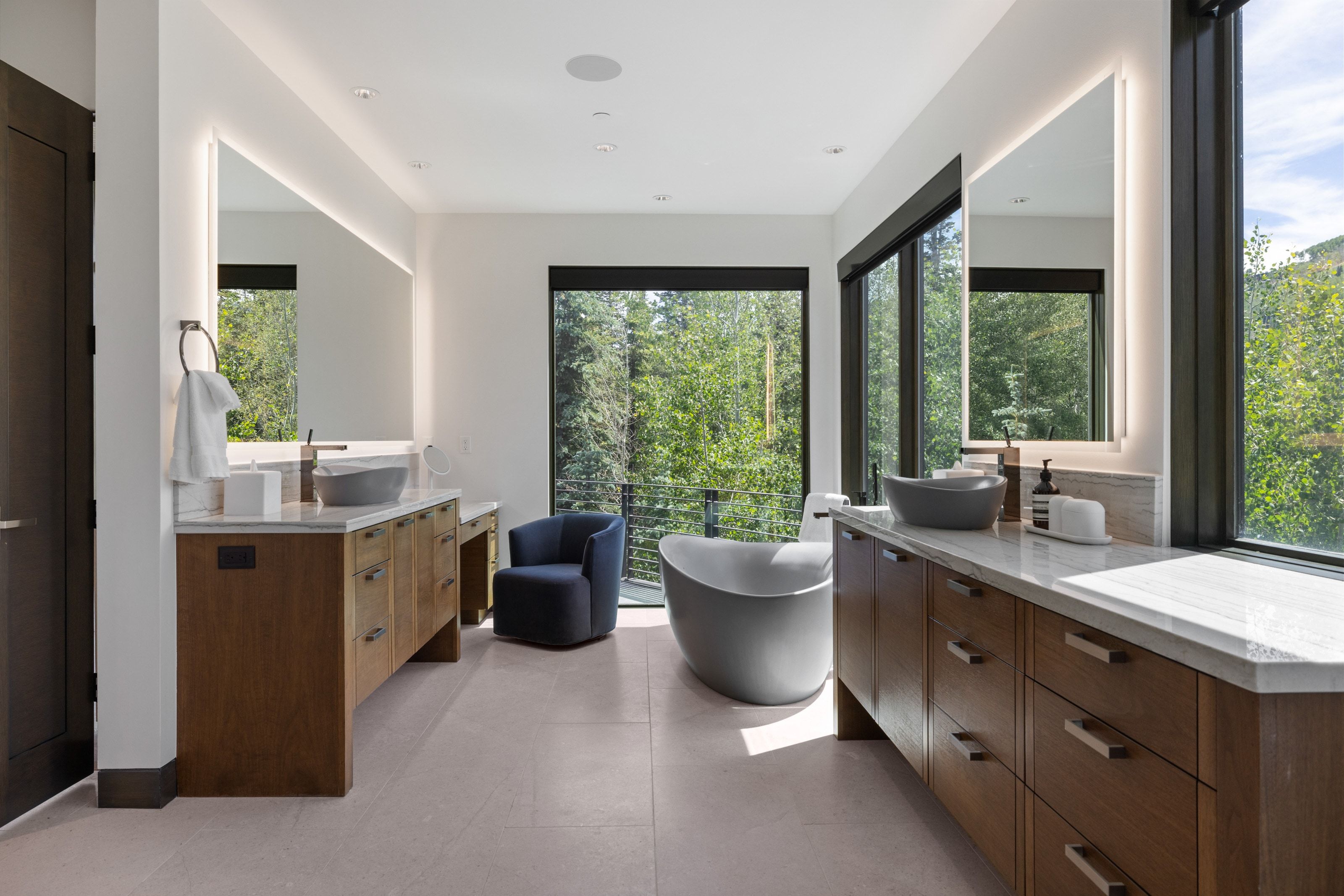 Spacious bathroom featuring a freestanding soaking tub, wood-finish double vanities with stone countertops, and large framed windows