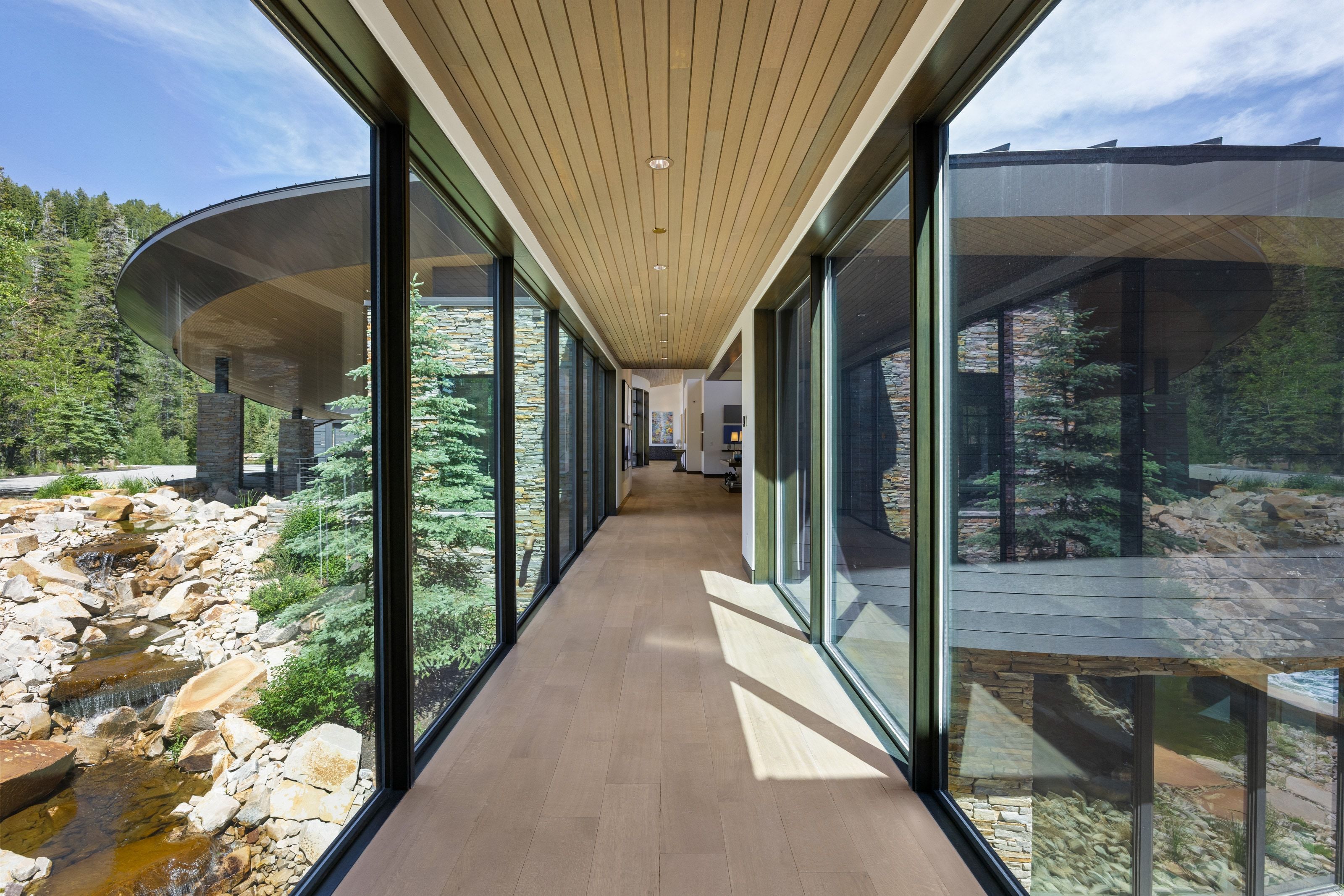 Glass-enclosed hallway with wood-finish flooring and a slatted wood ceiling