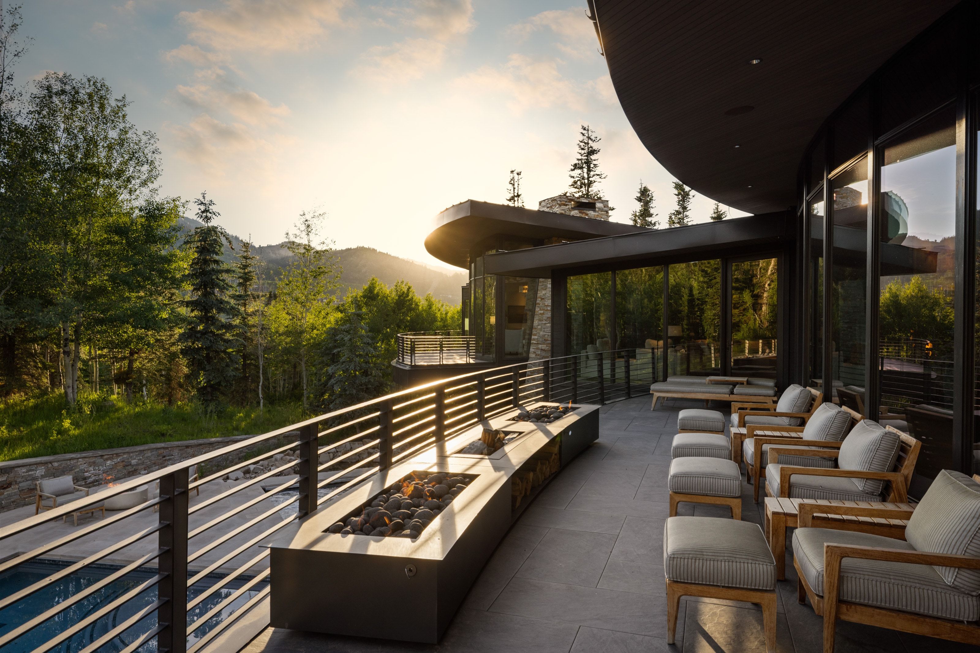 Expansive outdoor terrace featuring a built-in linear fire pit, a curved wall of full-height glass, and tile flooring