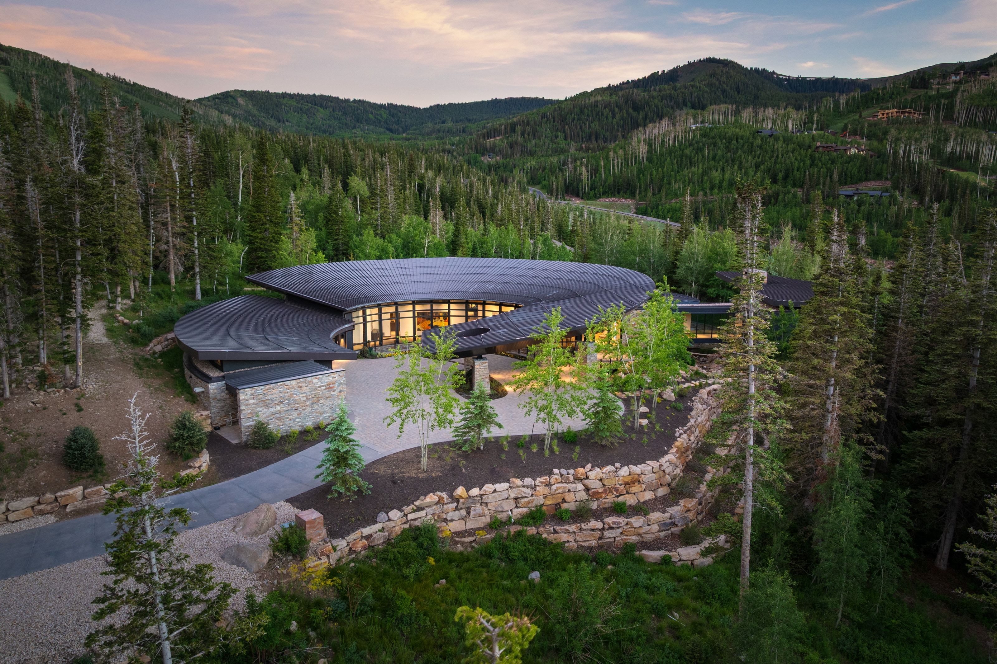 Contemporary architecture with a sweeping curved roofline, expansive window walls, and natural stone exterior elements