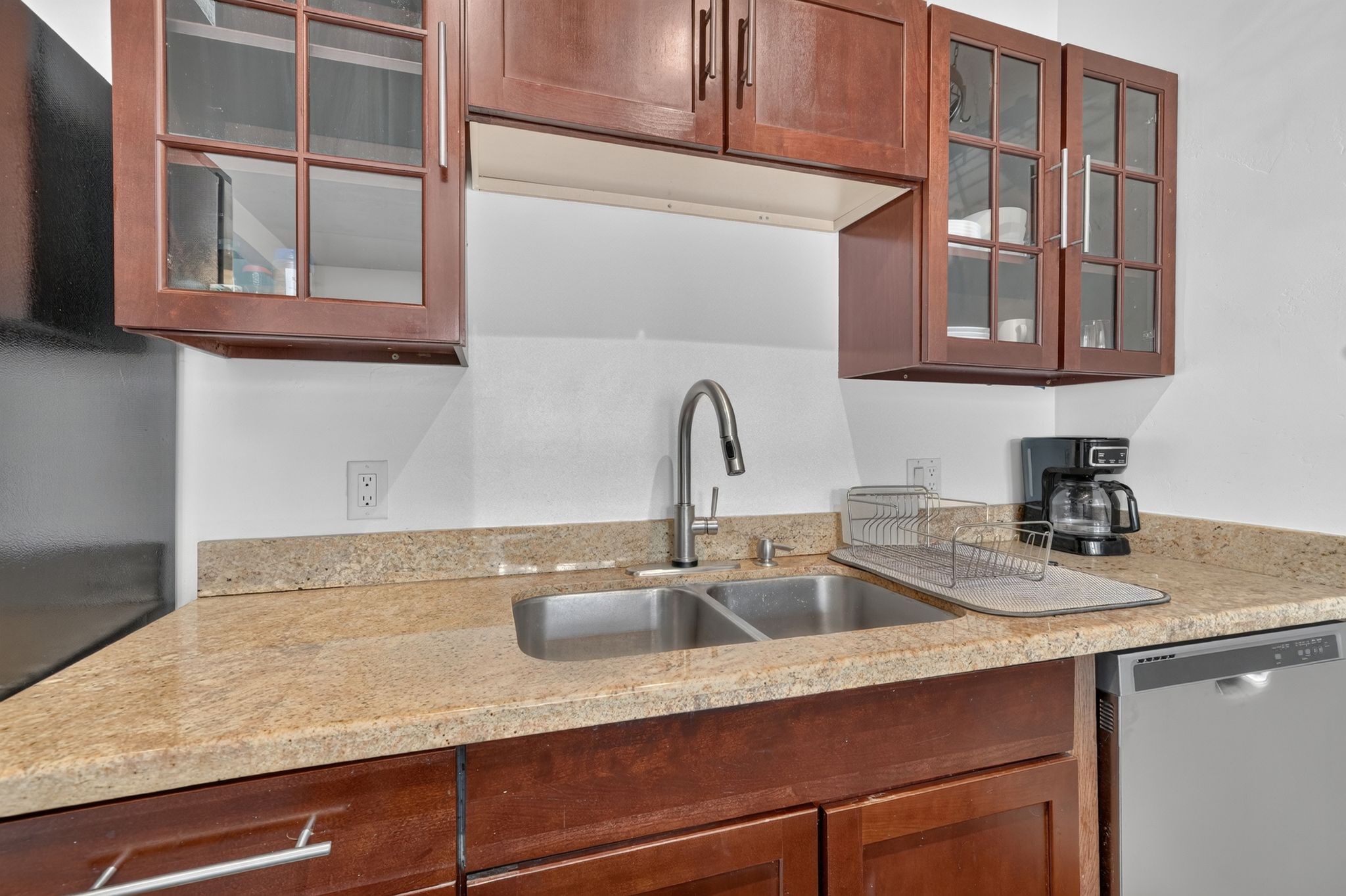 Kitchen featuring a double basin stainless steel sink with a gooseneck faucet, light granite-style countertops, wood cabinetry with glass-front uppers, and an integrated dishwasher