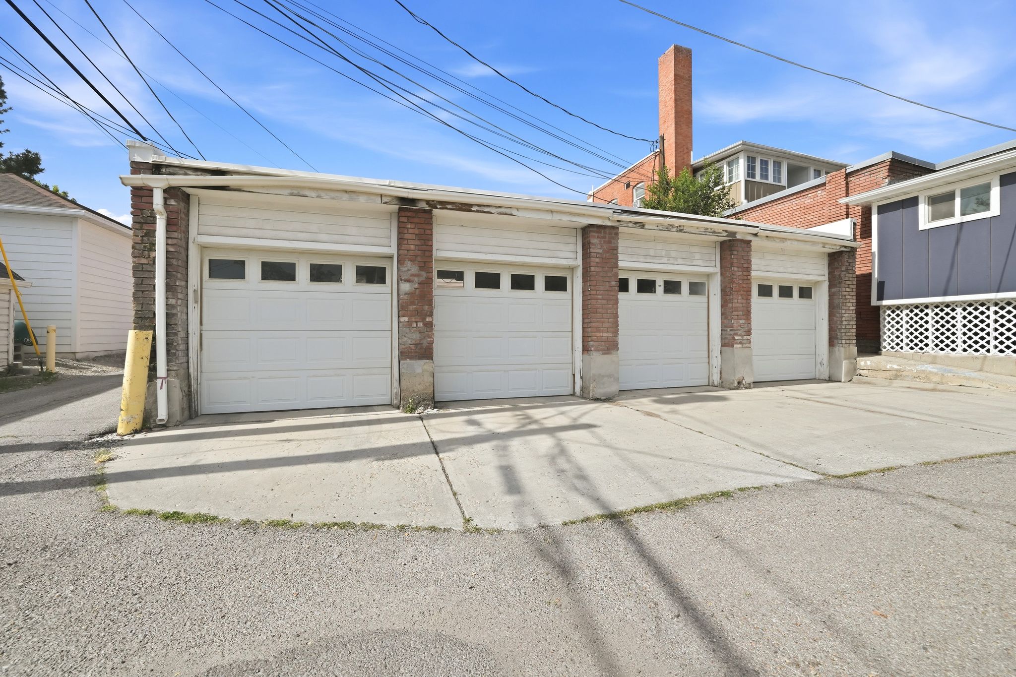 Four-bay garage structure featuring white panel garage doors with window inserts, brick pillar accents, and a concrete driveway apron