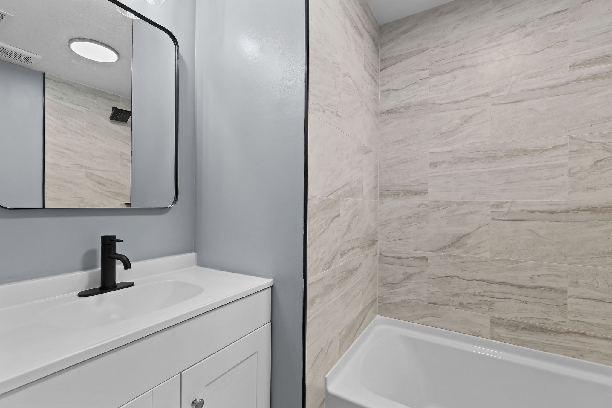 Bathroom featuring a white vanity with integrated sink, black single-handle faucet, and black-framed mirror