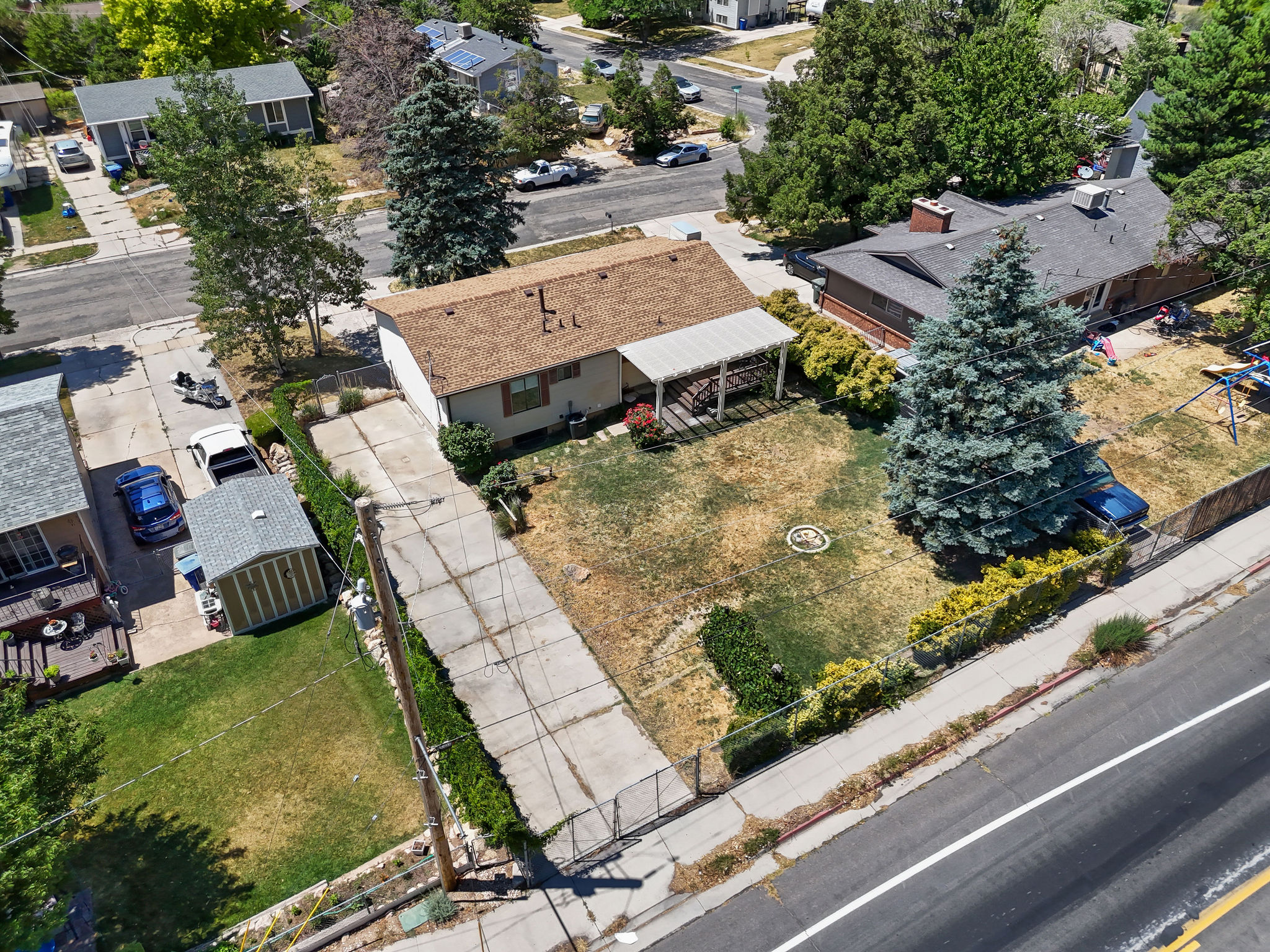 Expansive lot featuring a detached storage shed, paved driveway, mature trees, and a covered back patio