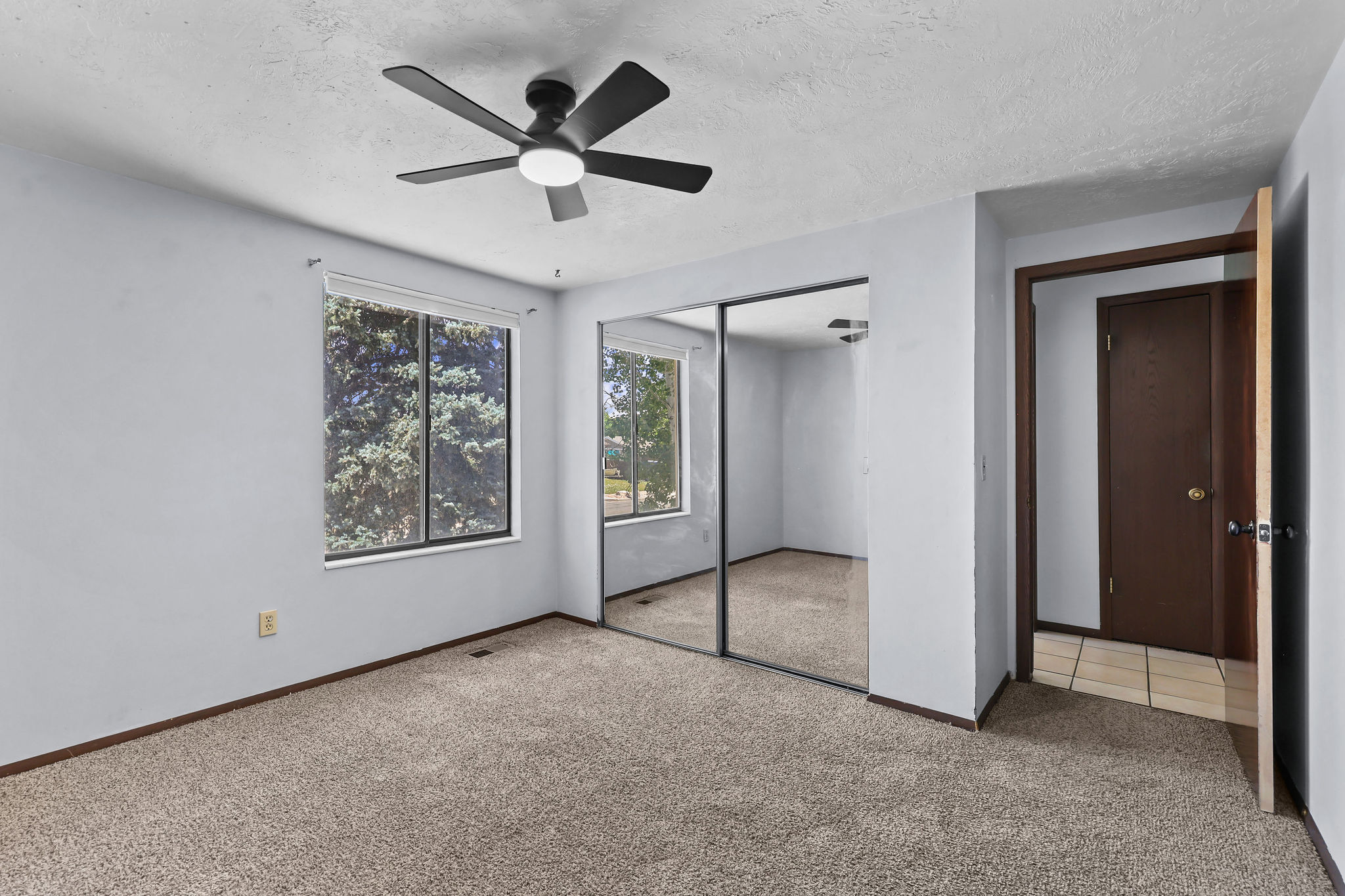 Carpeted interior space featuring a ceiling fan with integrated lighting, a broad window, and mirrored closet doors