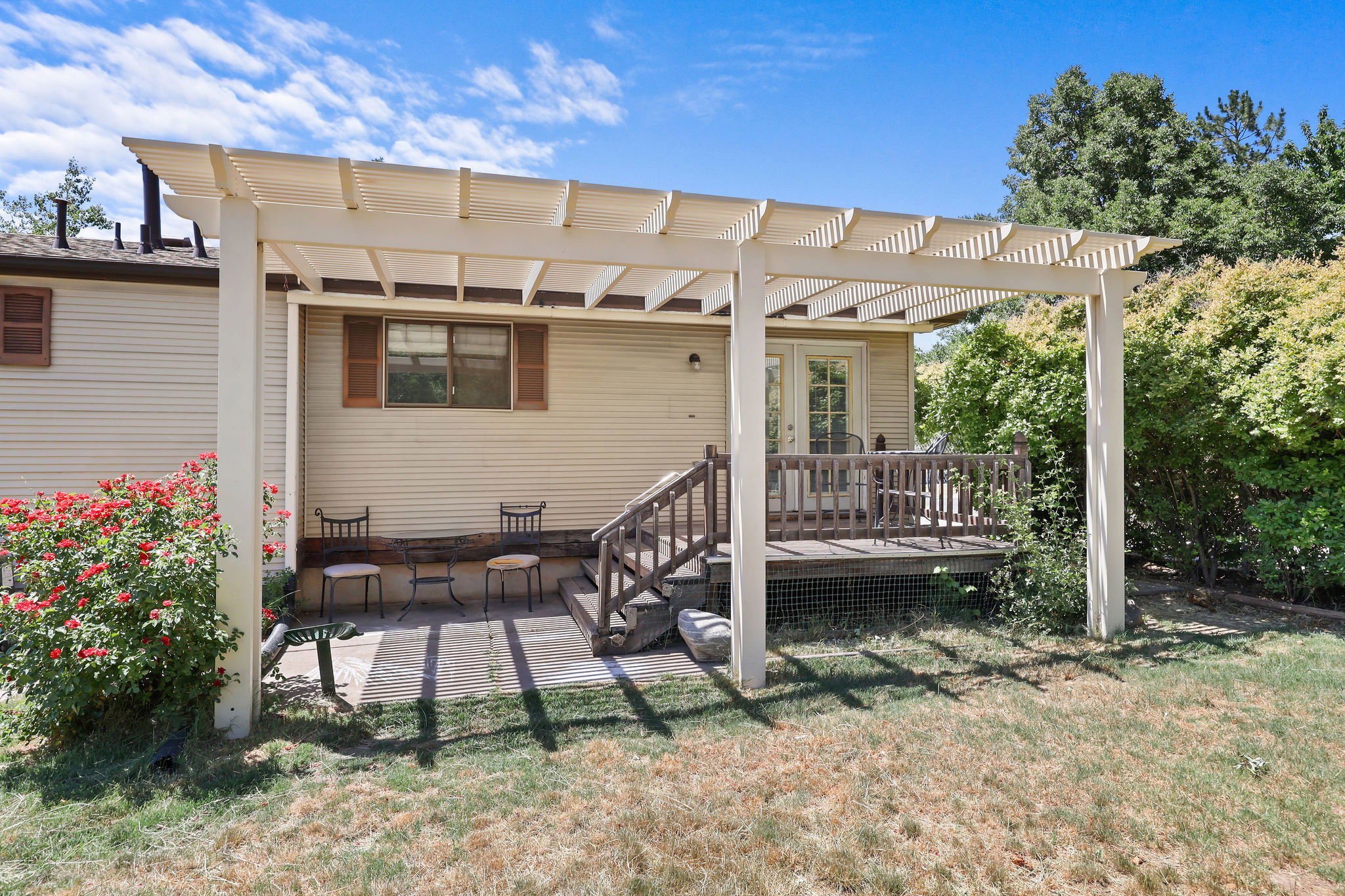 Expansive outdoor living area featuring a wooden pergola, an elevated deck with wood railing, and a ground-level patio