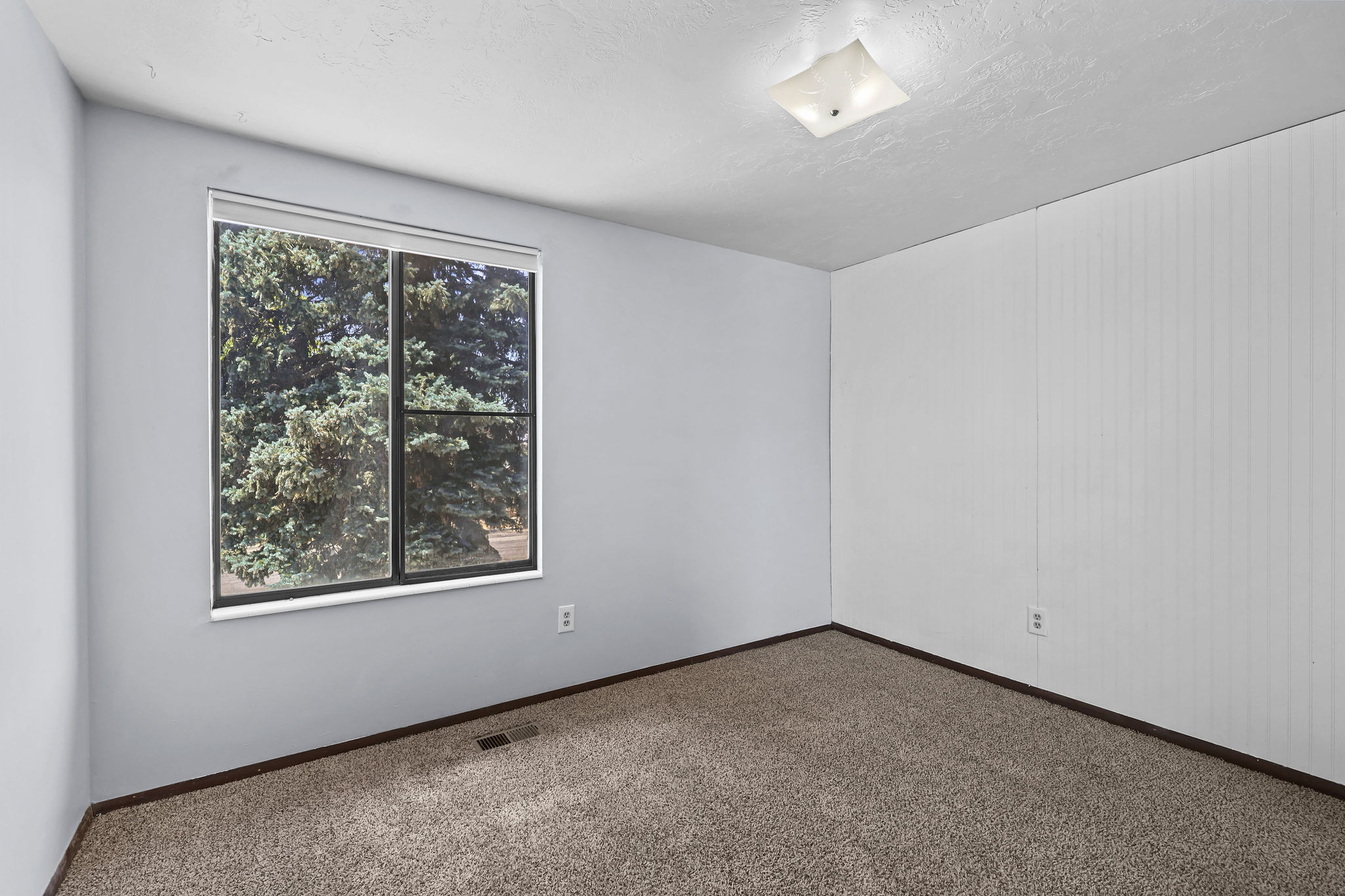 Room featuring a large window, textured ceiling, flush-mount lighting, light-toned carpeting, and a beadboard accent wall