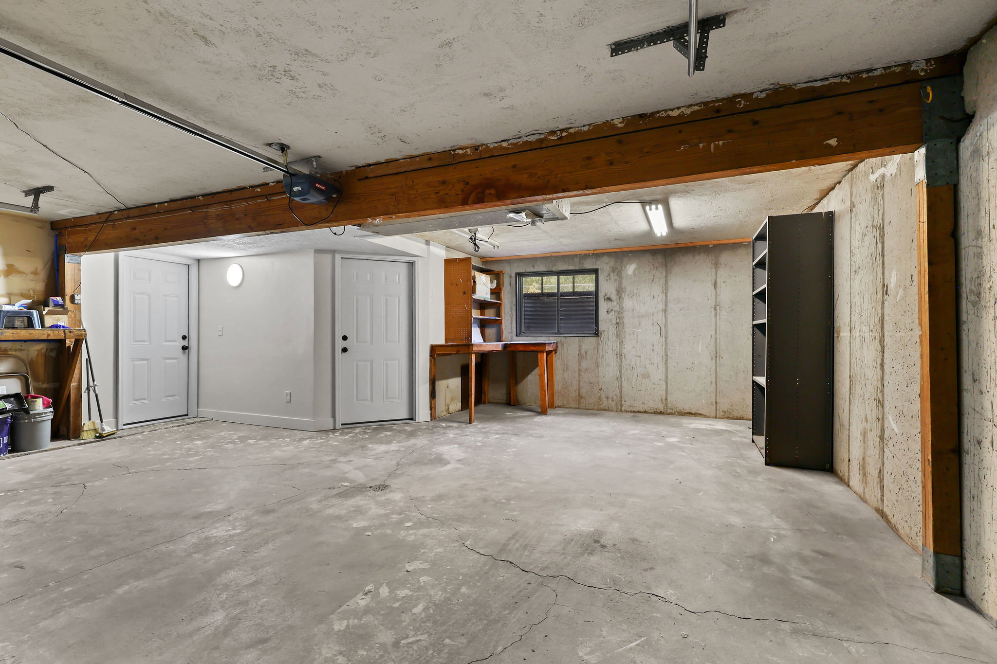 Spacious garage area featuring a concrete floor, exposed wooden beams, and multiple access doors