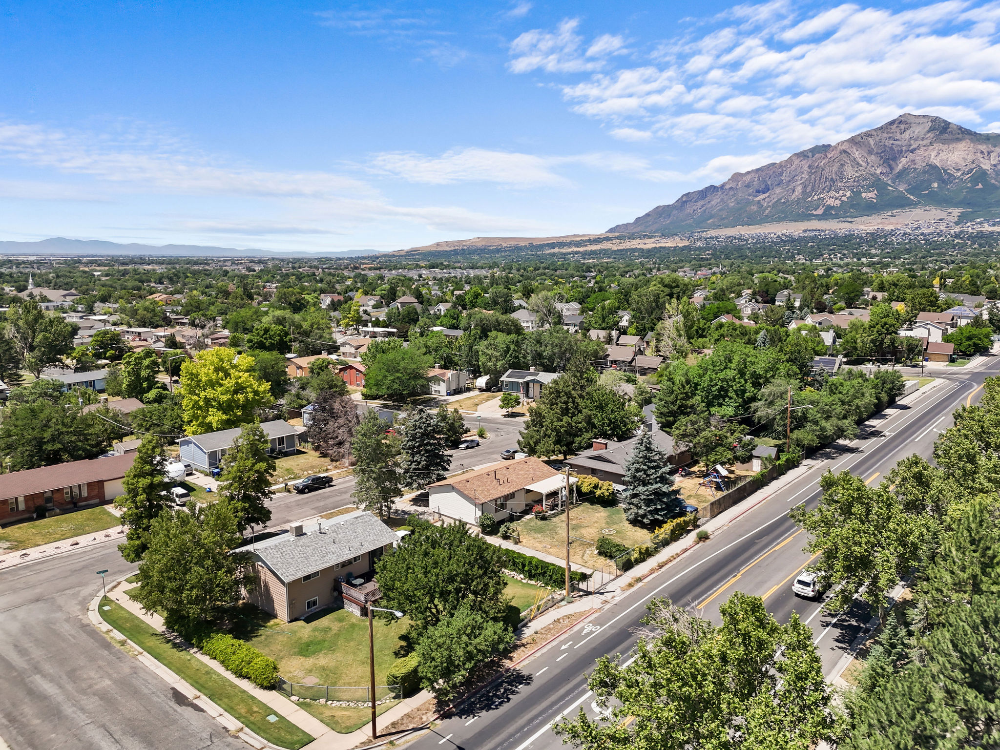 Expansive neighborhood featuring mature trees, residential properties, a paved road, and a distant mountain range