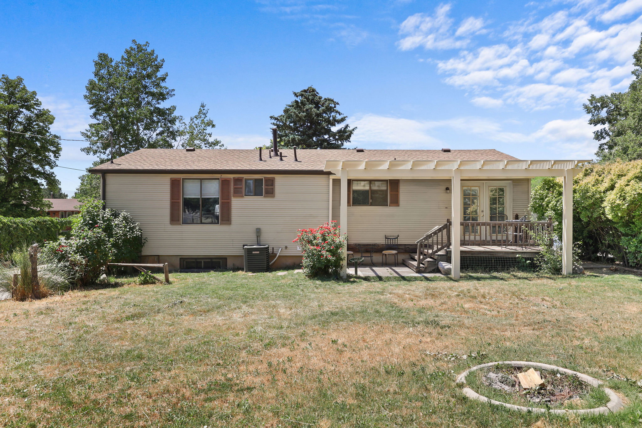 Backyard featuring a wood deck with a pergola, exterior siding, and mature trees