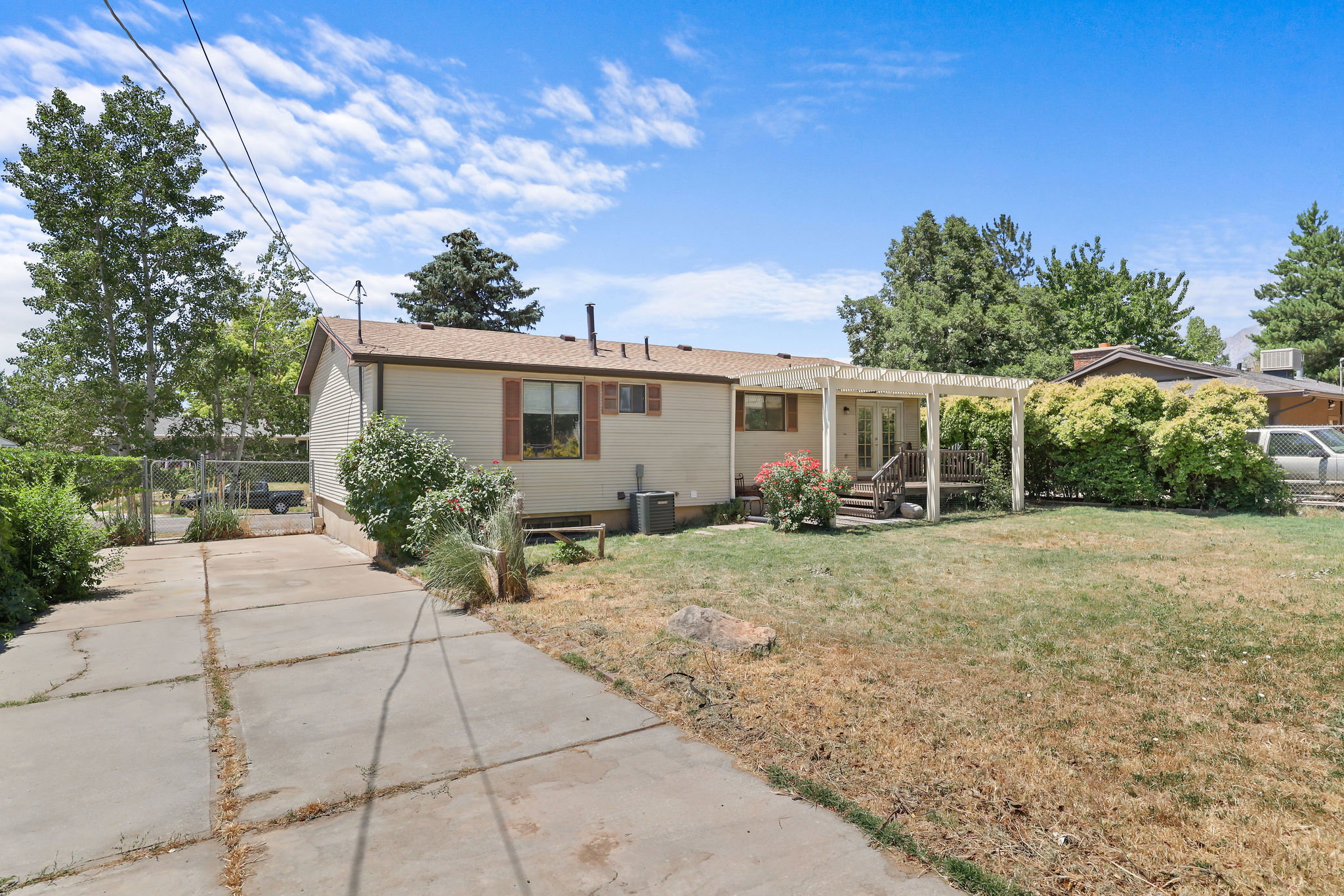 Expansive backyard featuring a concrete patio with a white pergola, mature landscaping, and established trees