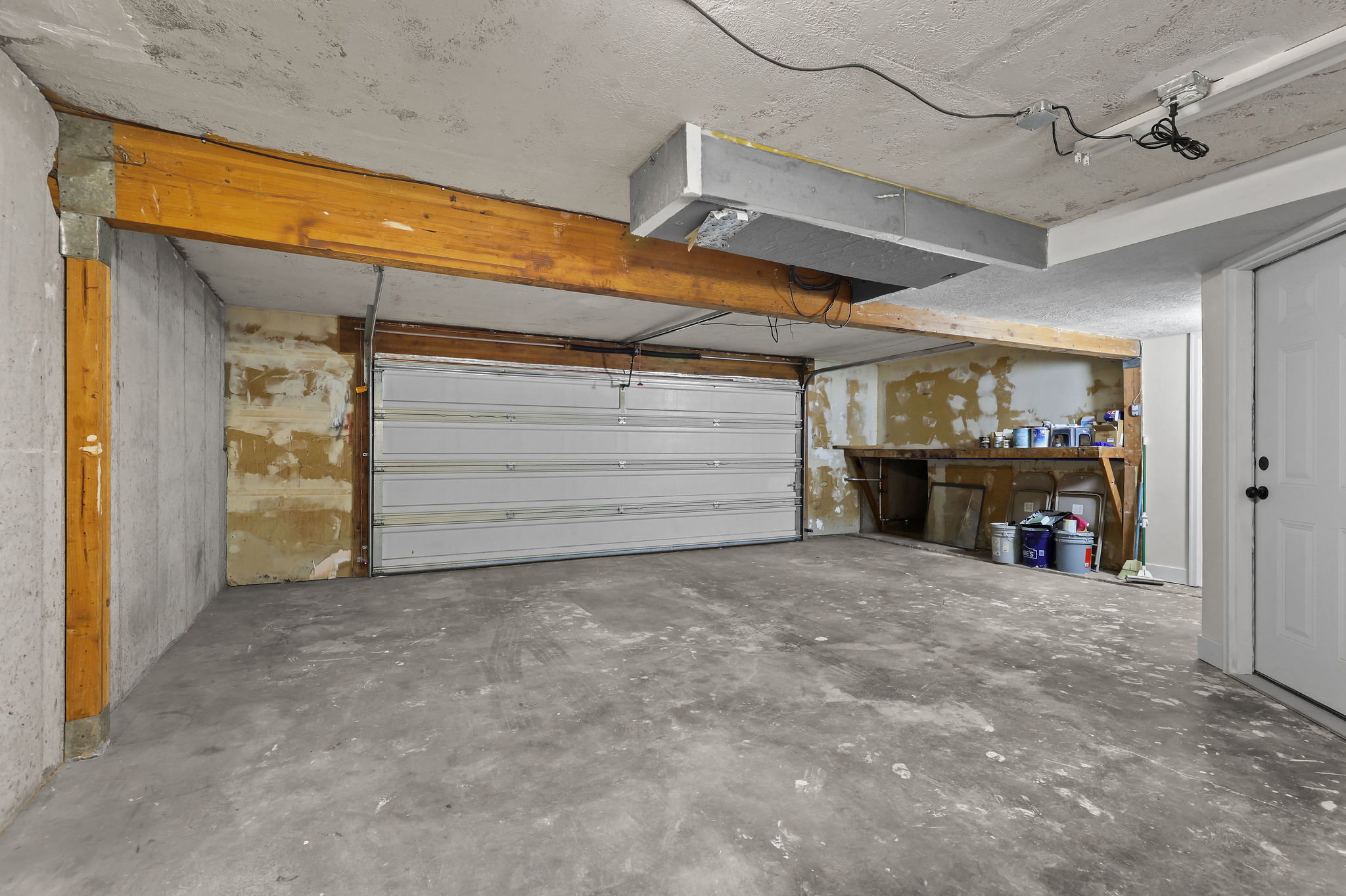 Concrete flooring with an overhead garage door, supported by a wooden beam structure