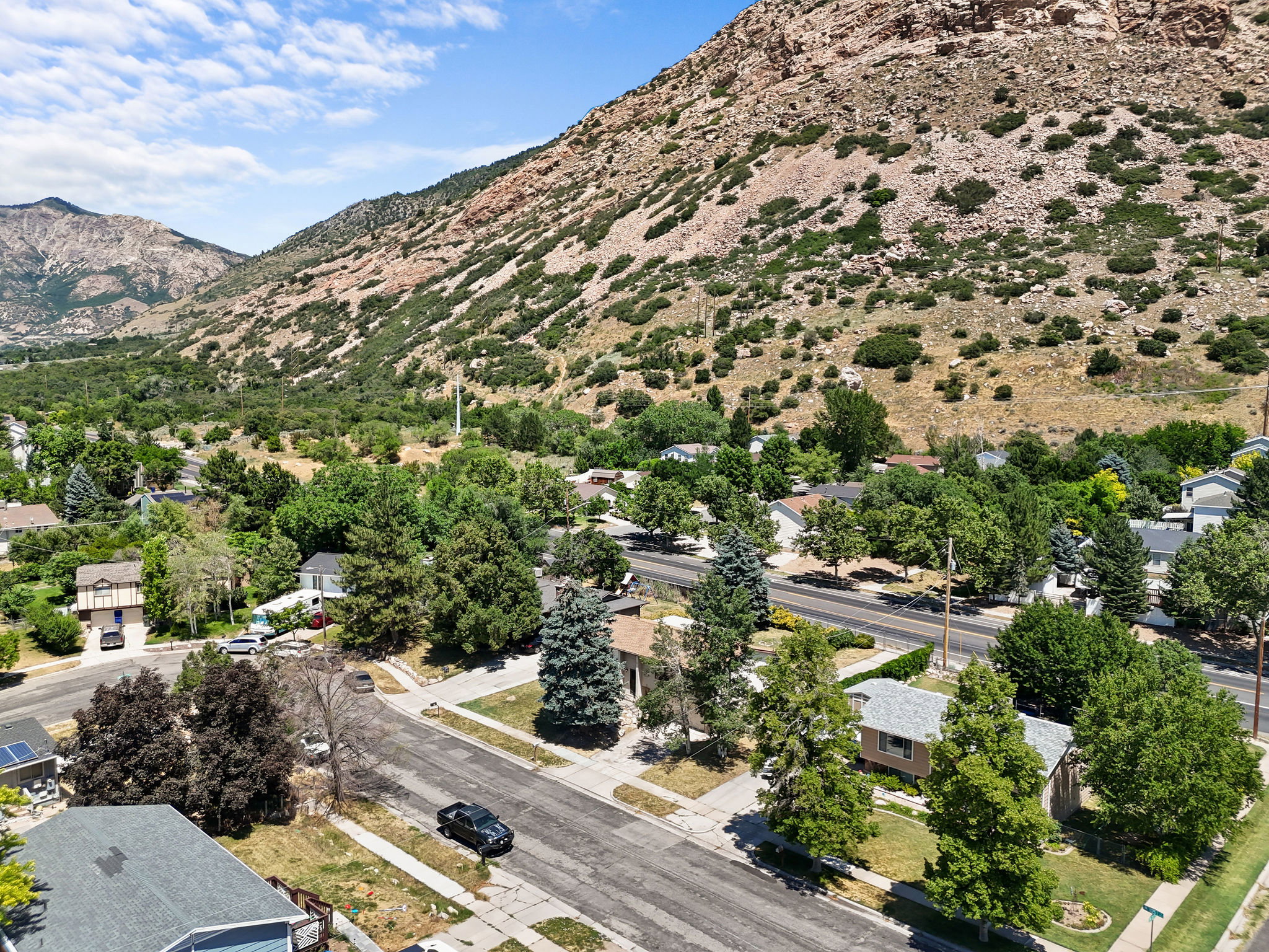 Aerial perspective of a neighborhood with diverse residential structures, abundant mature trees, and a prominent mountainous backdrop