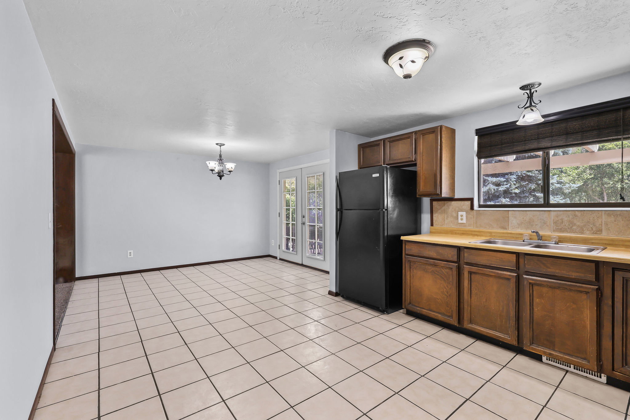 Kitchen featuring wood-finish cabinetry, tile countertops, tile backsplash, and a black refrigerator