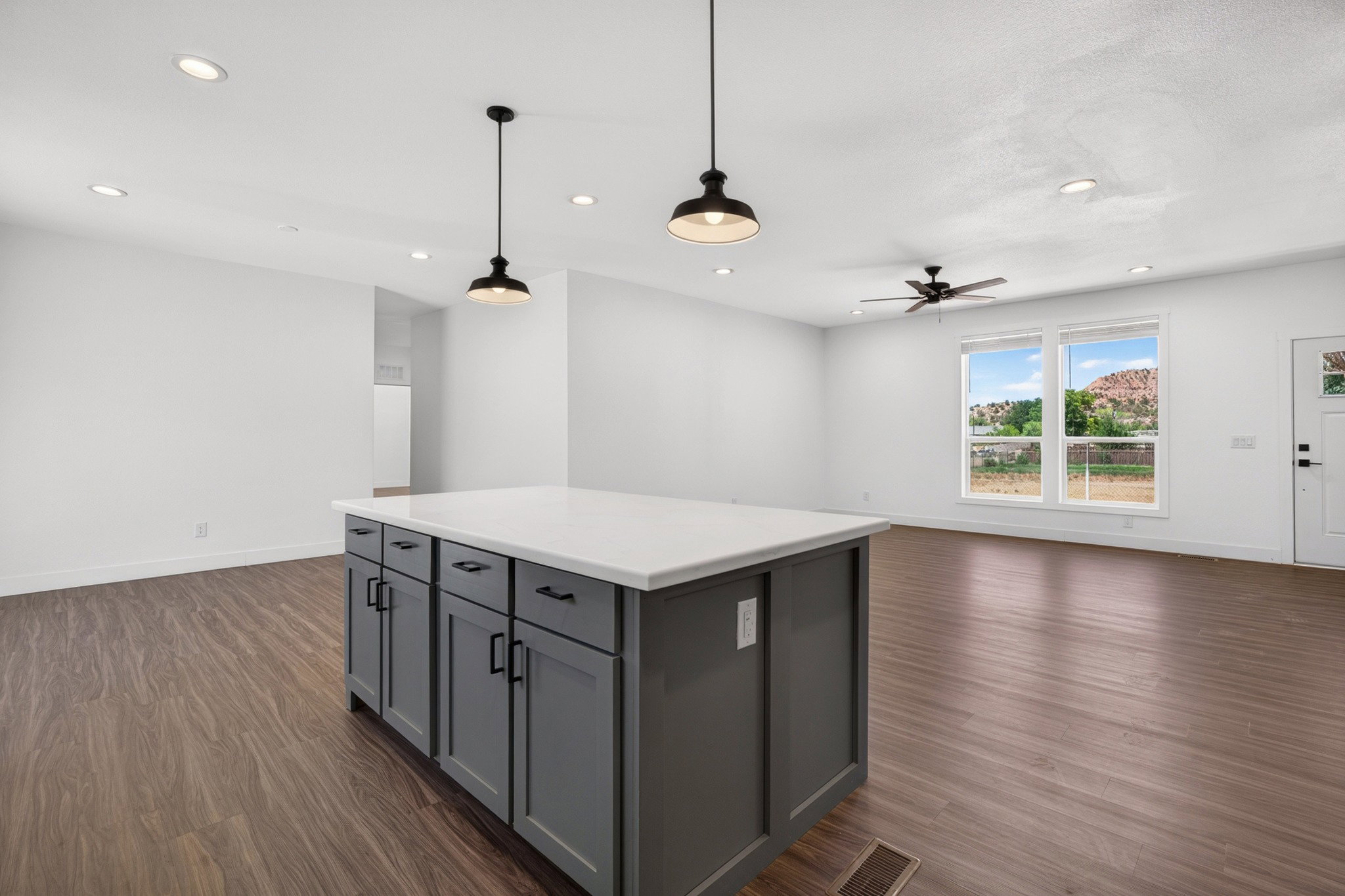 Kitchen island with a light-toned countertop and dark cabinetry, illuminated by two pendant lights and recessed ceiling lights