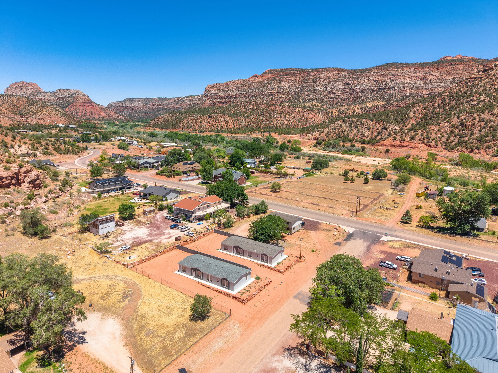 Expansive aerial perspective showcasing multiple properties amidst a desert landscape with prominent red rock formations in the background