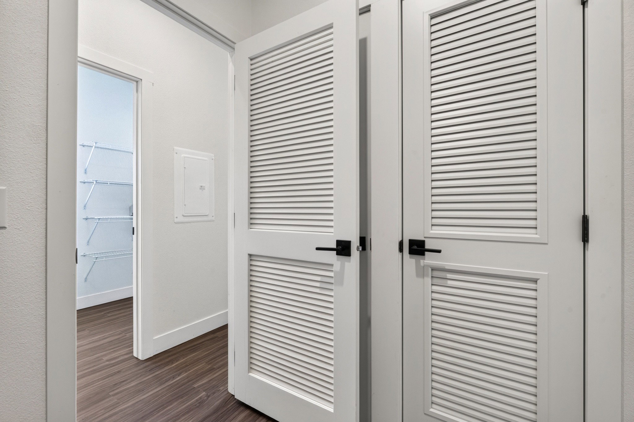 White louvered doors with matte black hardware, wood-finish flooring, and a walk-in closet featuring wire shelving