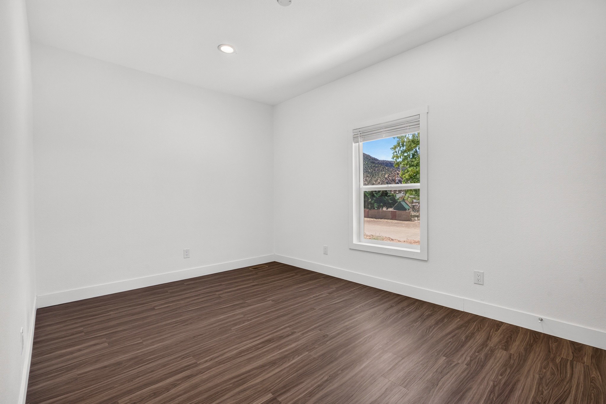 Room featuring wood-finish flooring, white walls, and a single window with blinds