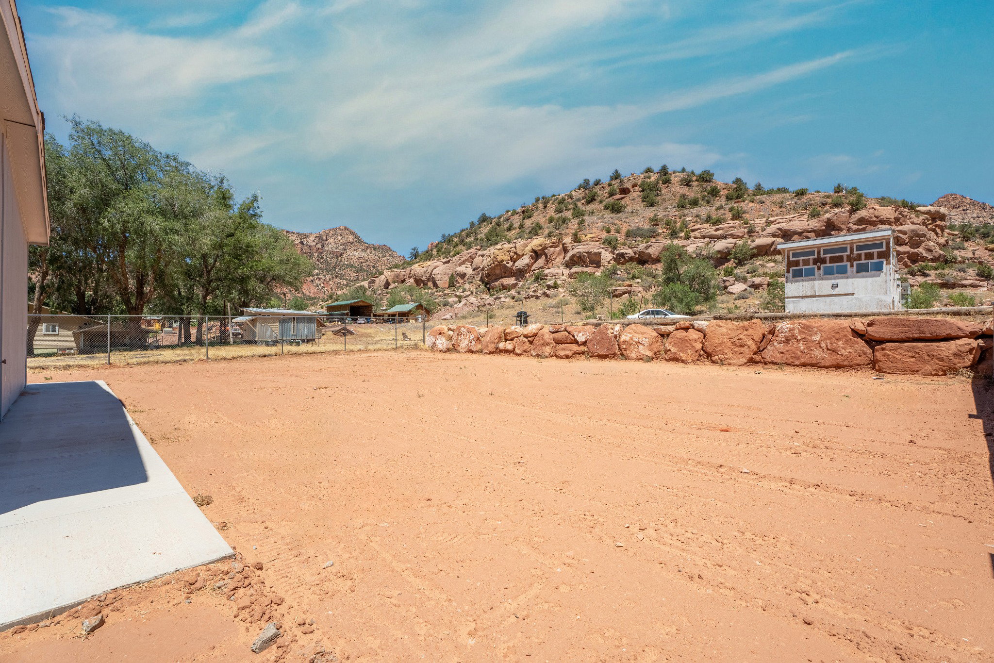 Expansive outdoor space featuring a large dirt area, a concrete patio, and a chain-link fence