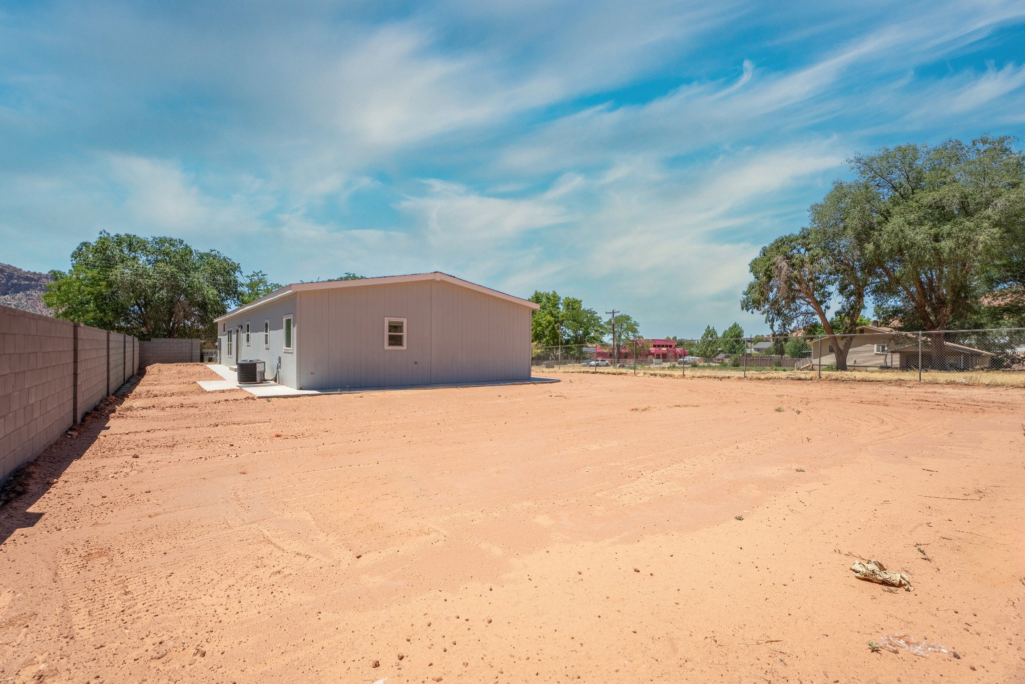 Expansive rear yard with a neutral-toned block perimeter wall and a large area of undeveloped land