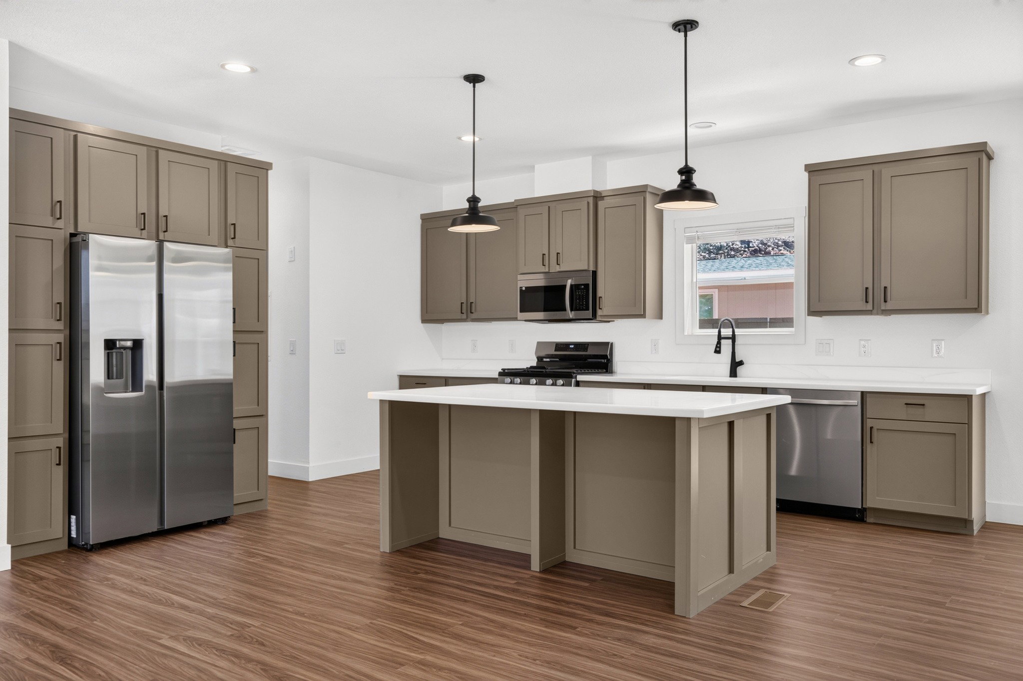 Kitchen with a center island, warm-toned cabinetry, stainless steel appliances, white countertops, and wood-finish flooring