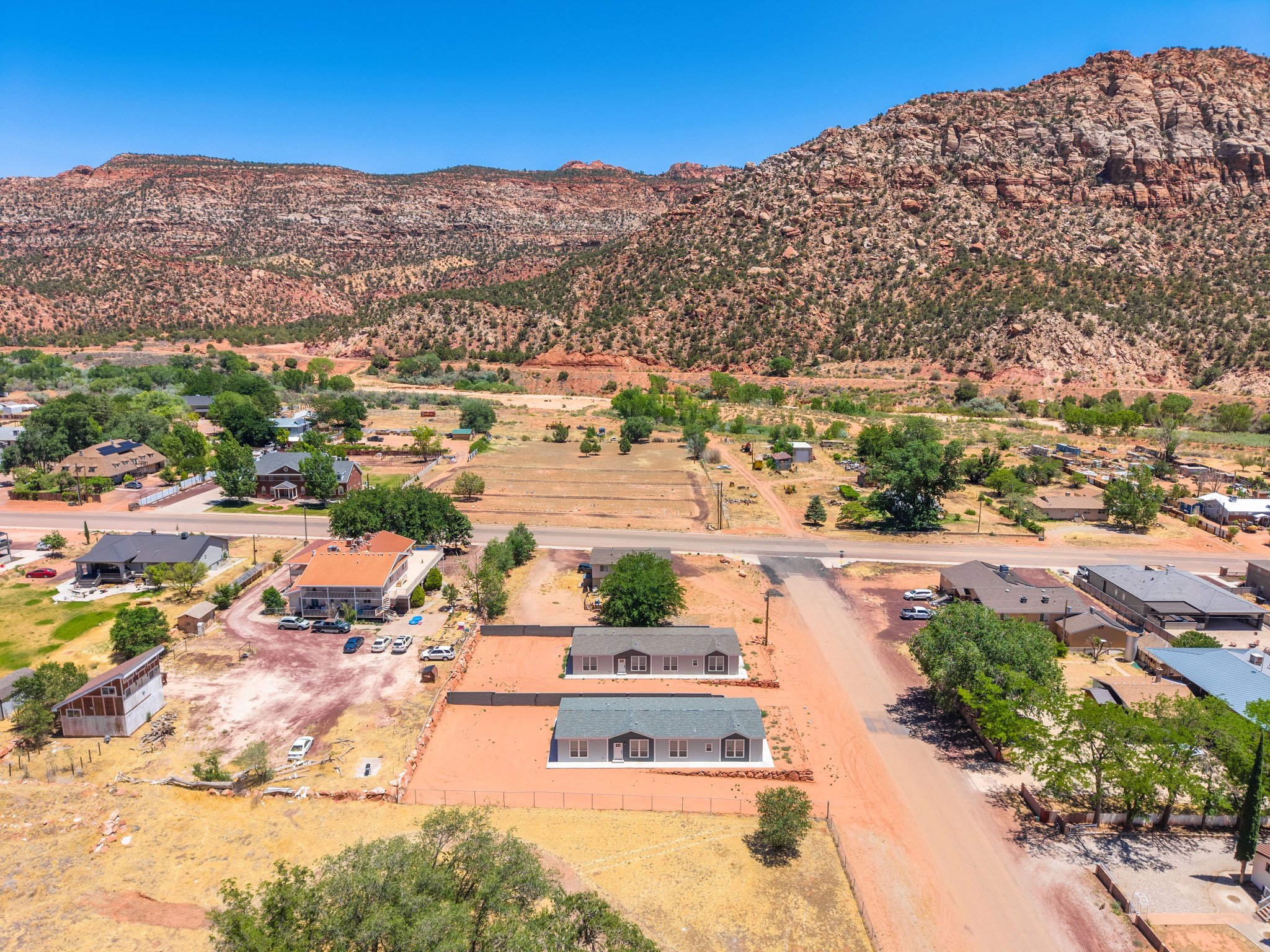 Aerial perspective featuring two light-colored residences with dark roofs, set against a backdrop of natural red rock formations and scattered greenery