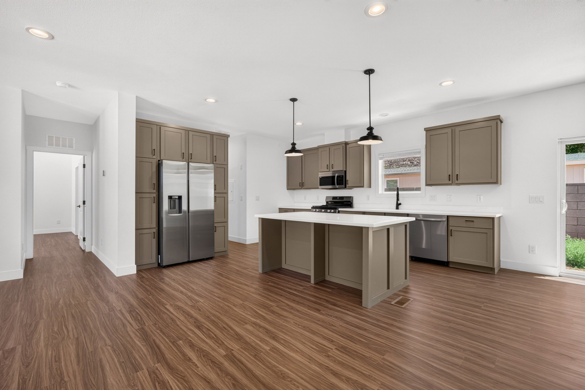 Open-concept kitchen featuring wood-finish flooring, recessed lighting, a central island with a solid surface countertop, matte gray cabinetry, and stainless steel appliances
