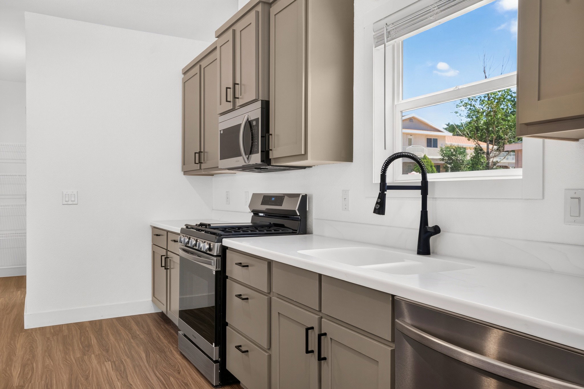 Kitchen featuring wood-finish flooring, light grey cabinetry, white countertops, stainless steel appliances, and a black gooseneck faucet