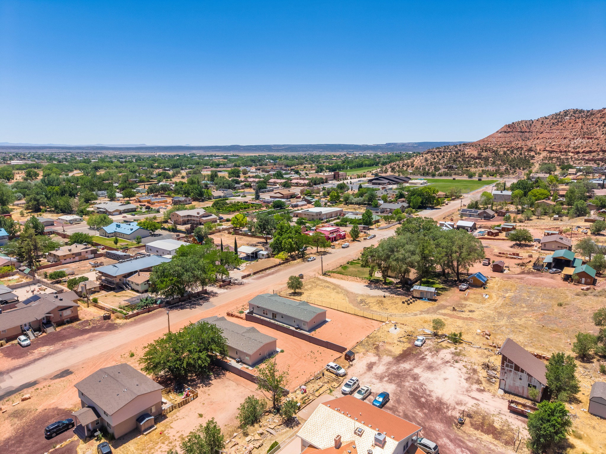 Aerial perspective showcasing a residential landscape with varied housing styles and mature trees, framed by distant hills and a clear sky